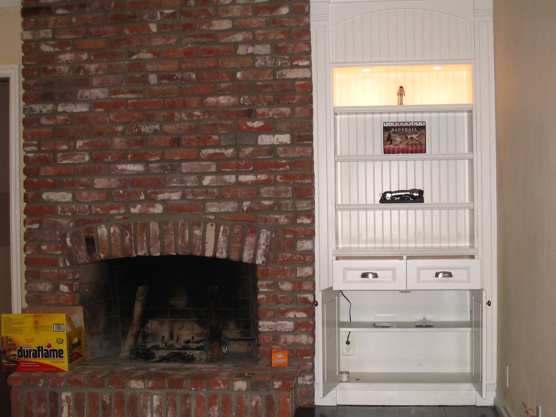 Brick fireplace with built-in white shelving unit. Open cabinet doors, items on shelves.