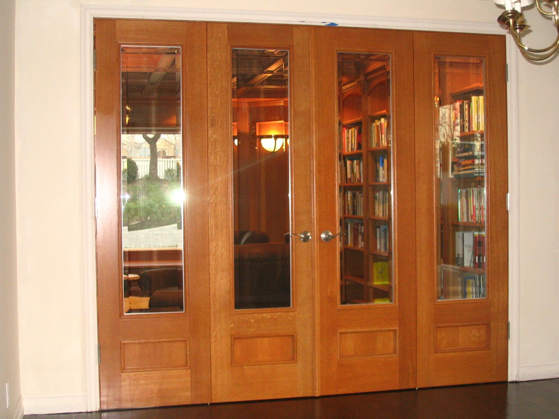 Four wooden glass-paned doors, two open, revealing a library with bookshelves and furniture.