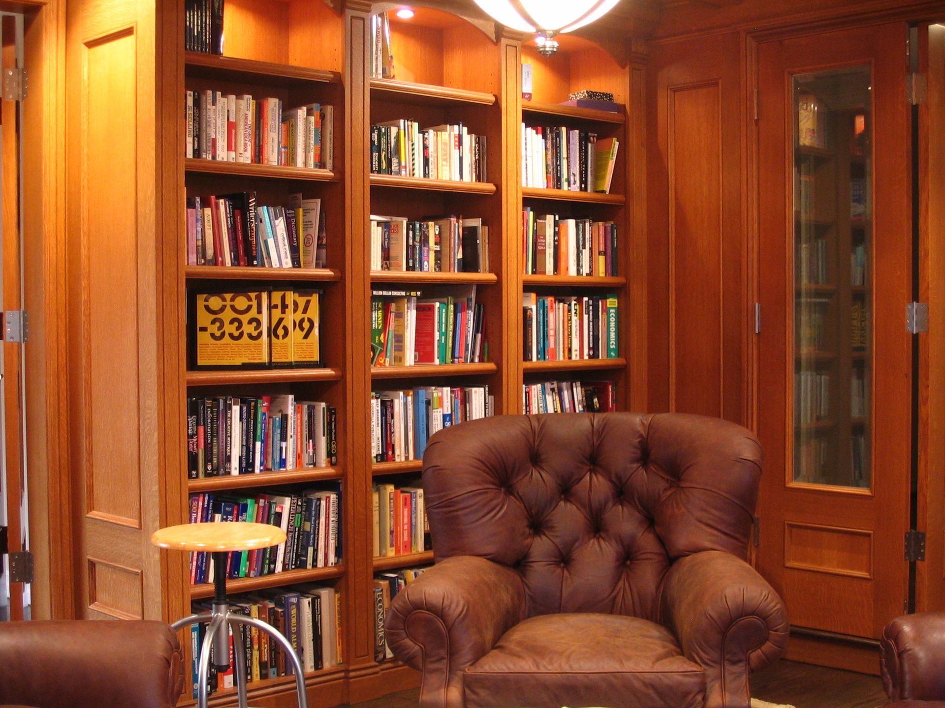 Cozy library with built-in bookshelves, leather armchair, small table, and a door, all framed in warm wood tones.