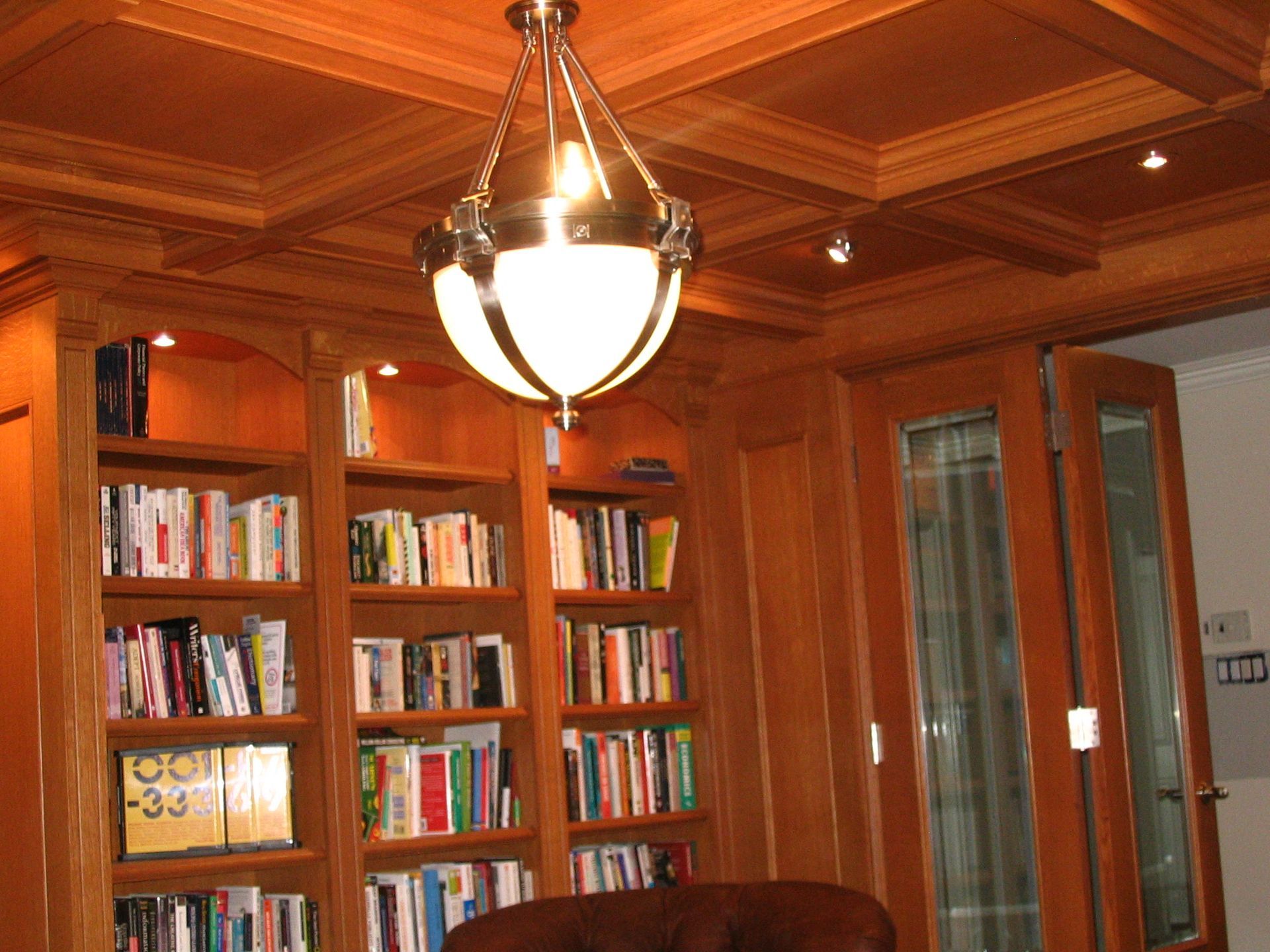 Wooden library with built-in bookshelves, ceiling light, and double doors; books fill the shelves.