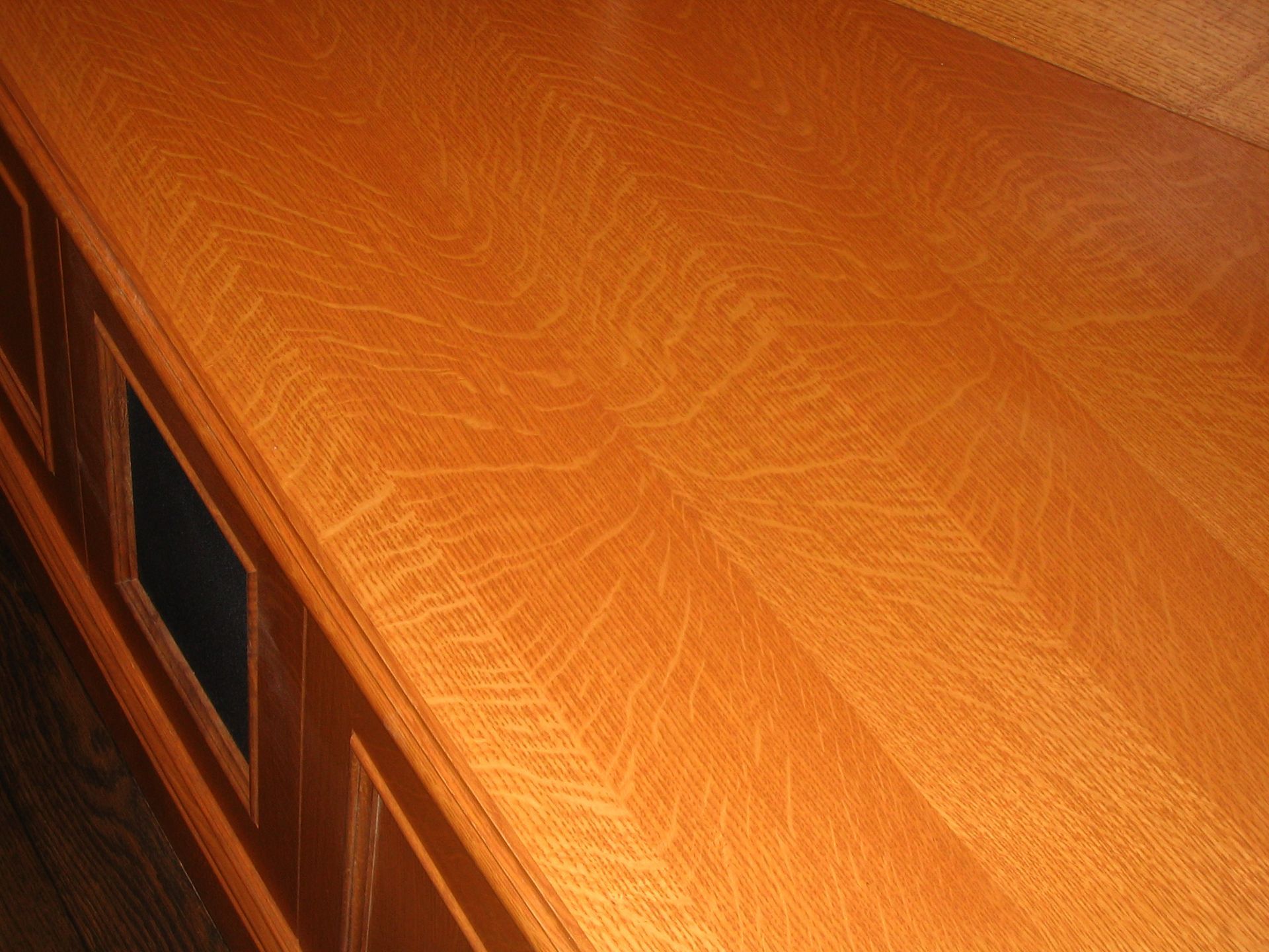 Close-up of a wooden surface showing a distinctive grain pattern. The wood is finished with a warm, amber tone.