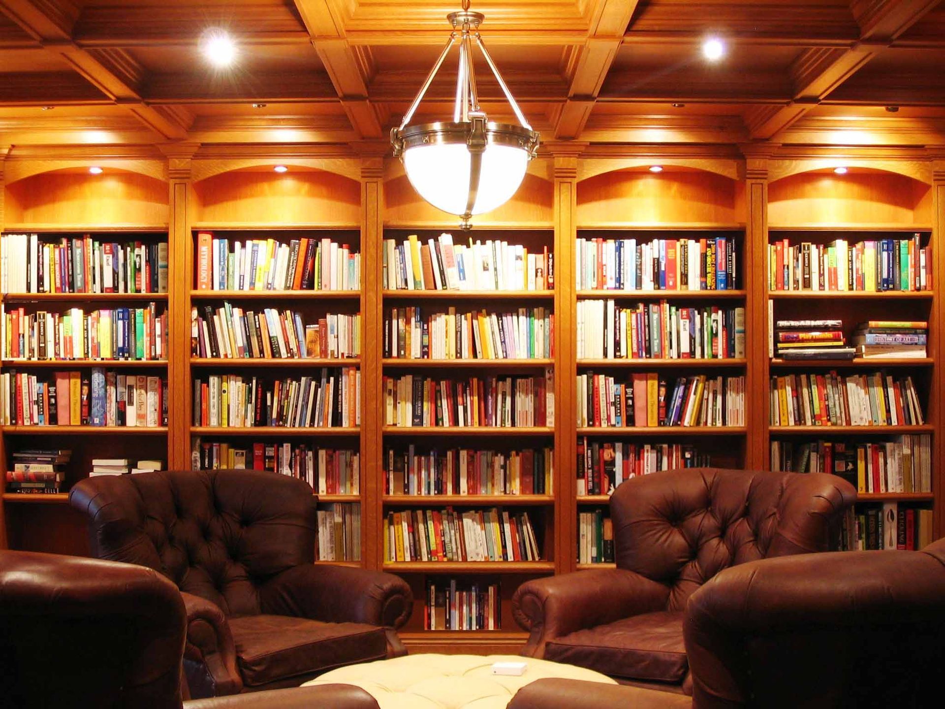 Cozy library with leather chairs and bookshelves filled with books. Warm lighting illuminates the wood paneling.