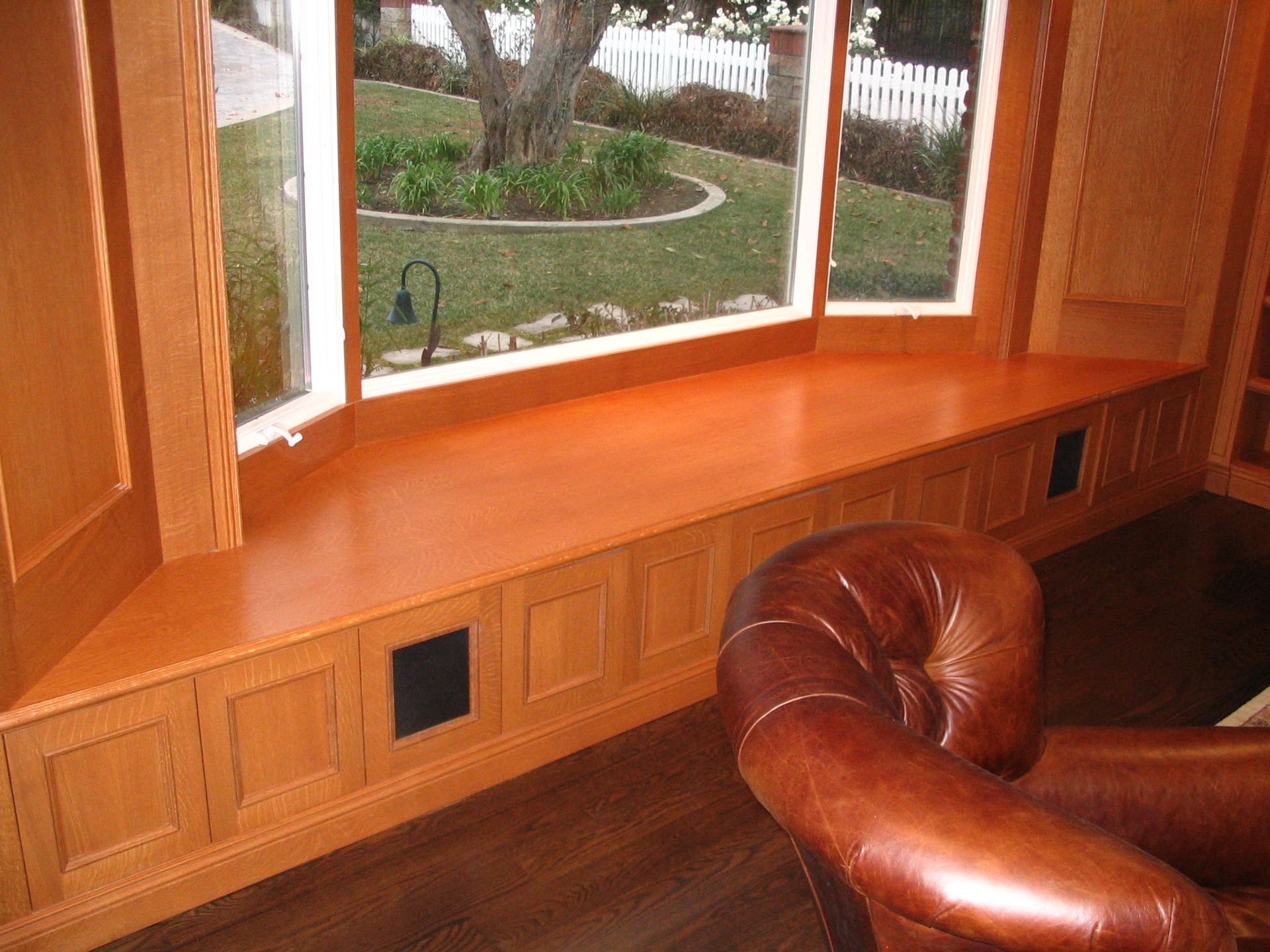 Bay window with wooden bench, leather armchair, and view of a lawn and white fence.