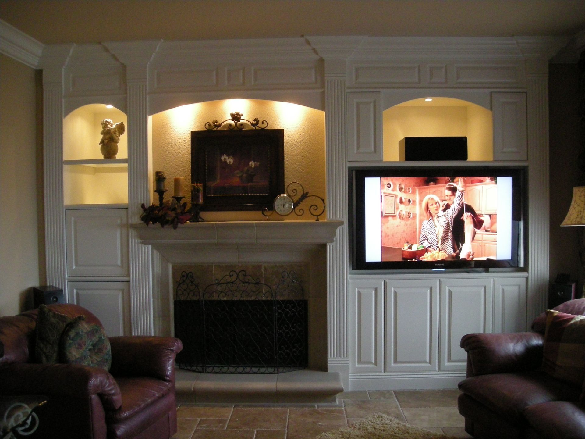 Living room with fireplace, built-in shelves, TV. Red leather chairs. Beige and brown tones.