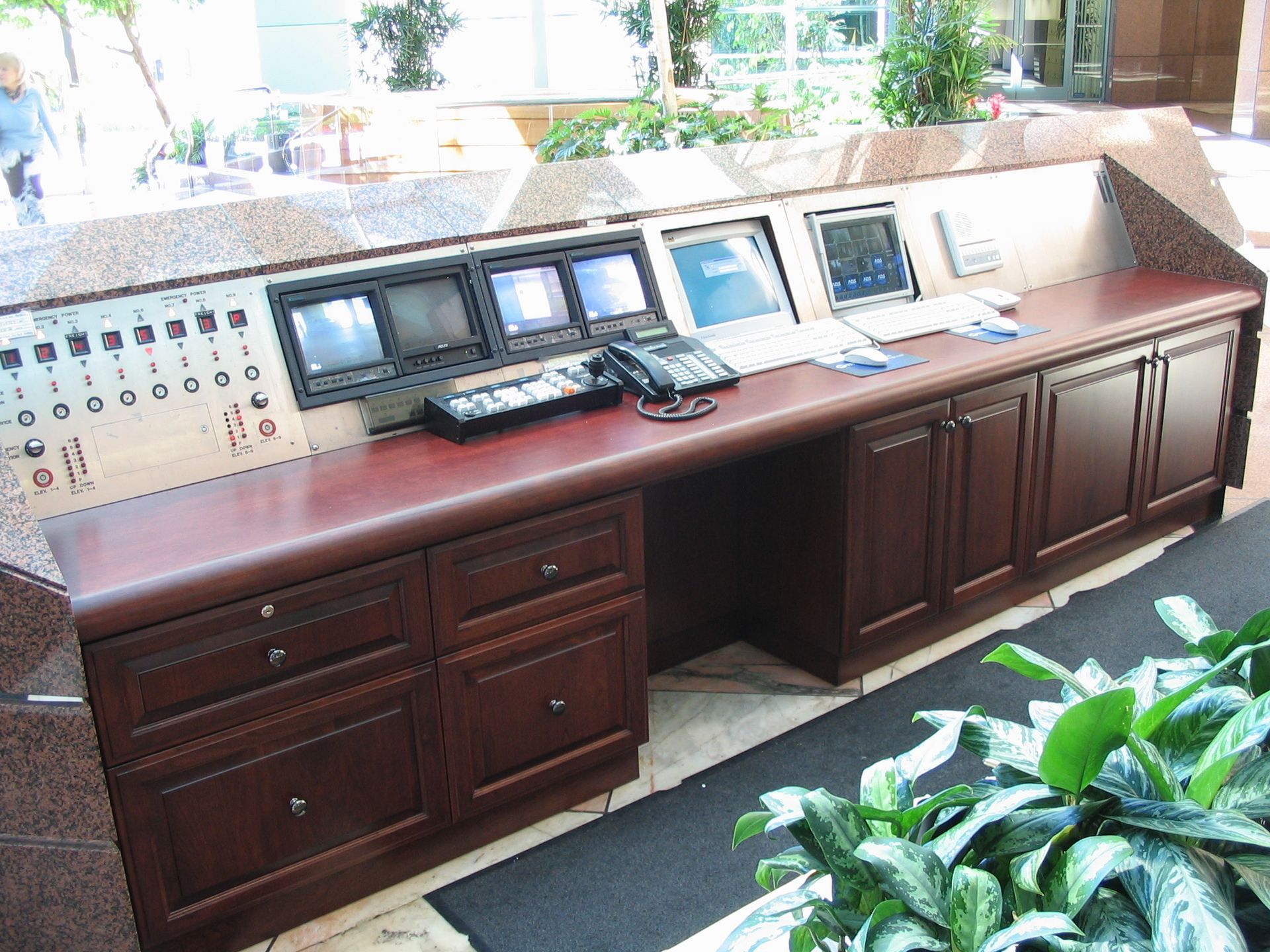 Control desk with monitors, buttons, drawers, and cabinets in an office setting.