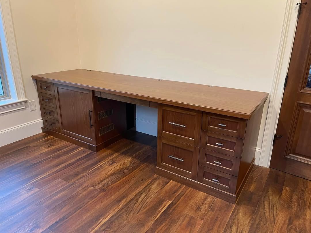 Wooden desk against a light wall, with drawers and cabinet, on a wood floor.