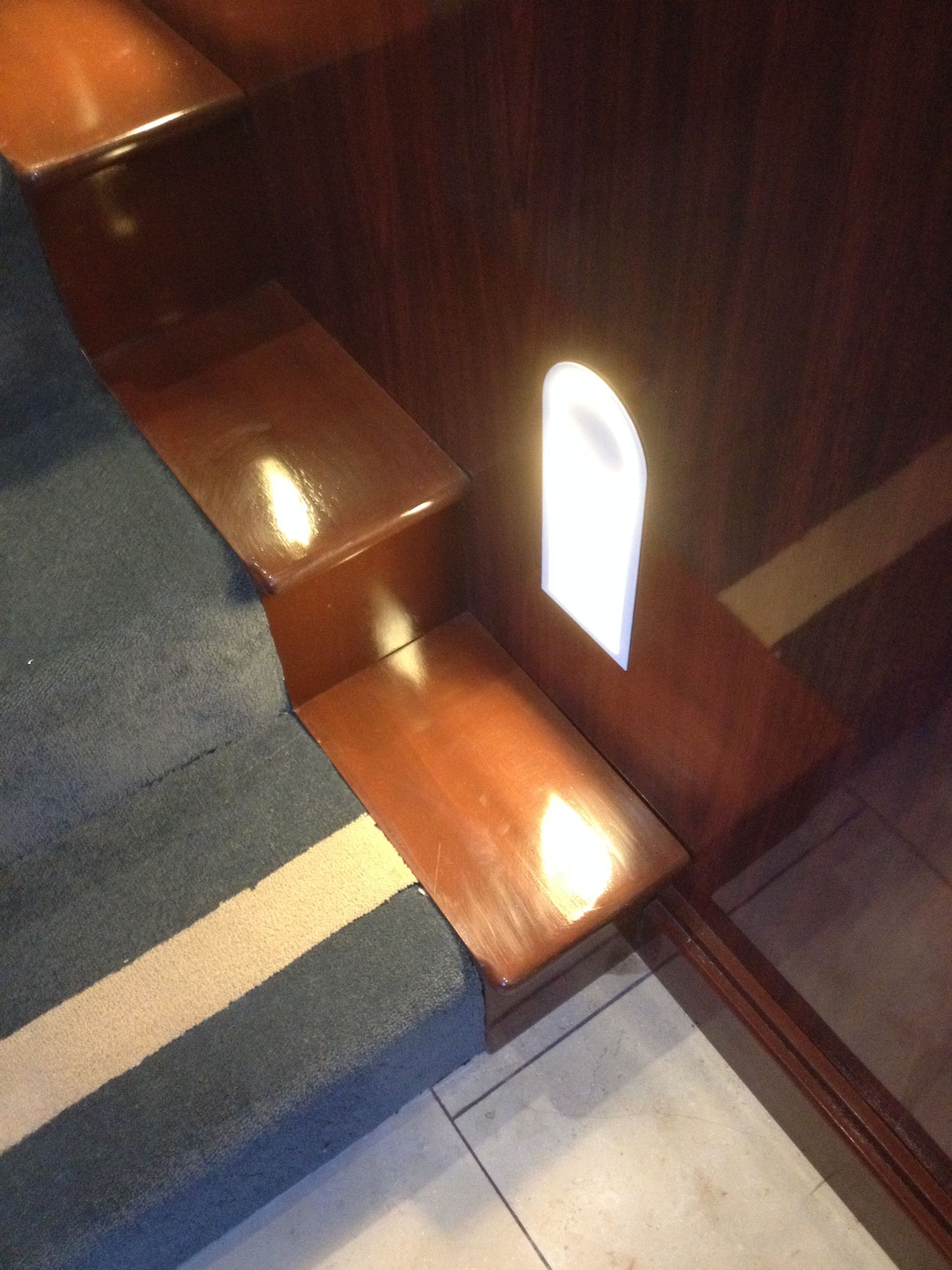 Wooden steps with a blue and white carpet runner. A bright light shines from a small arched opening.