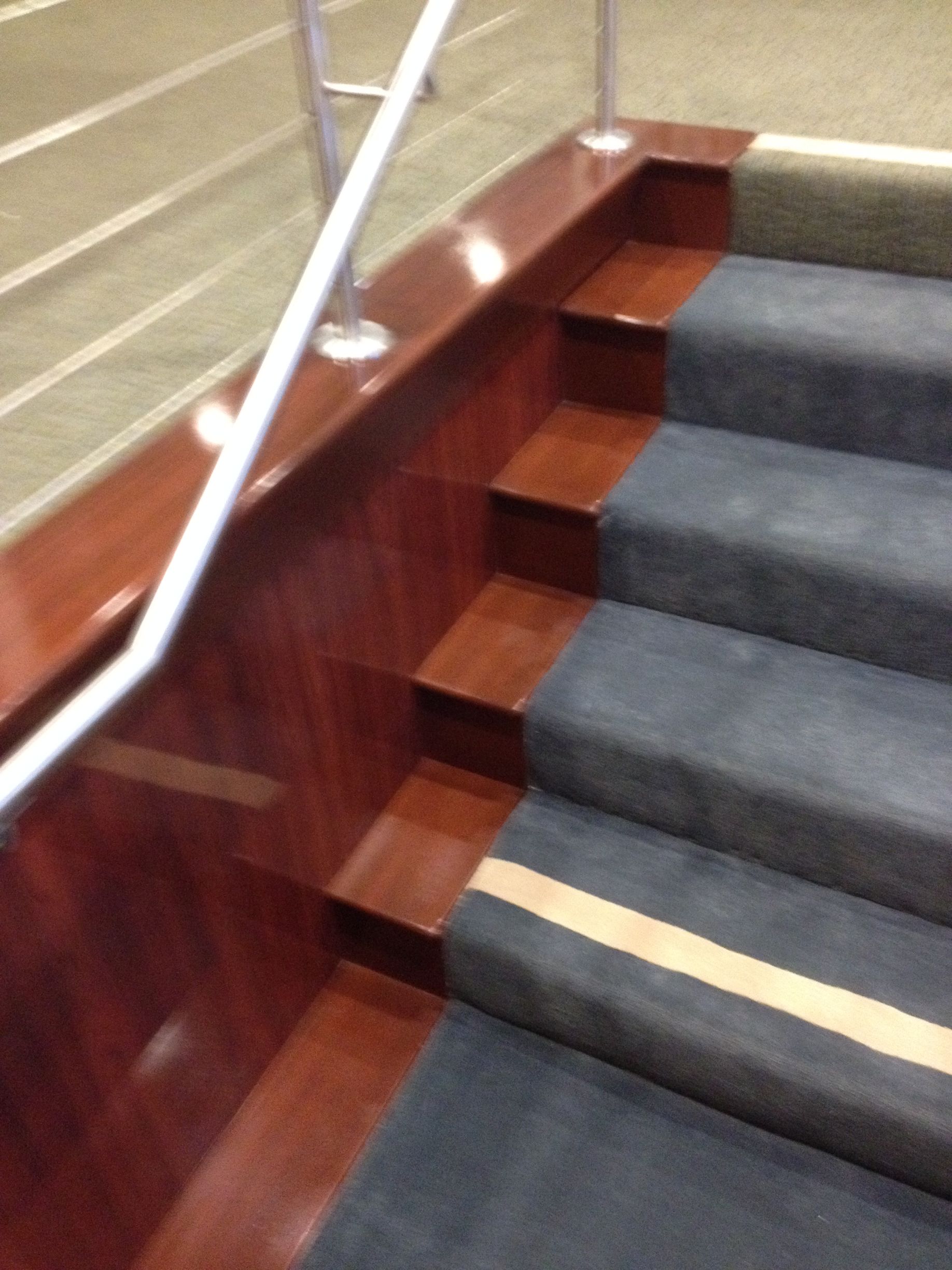 Wooden and carpeted staircase with a handrail. Dark wood trim and gray carpet with a yellow stripe on each step.