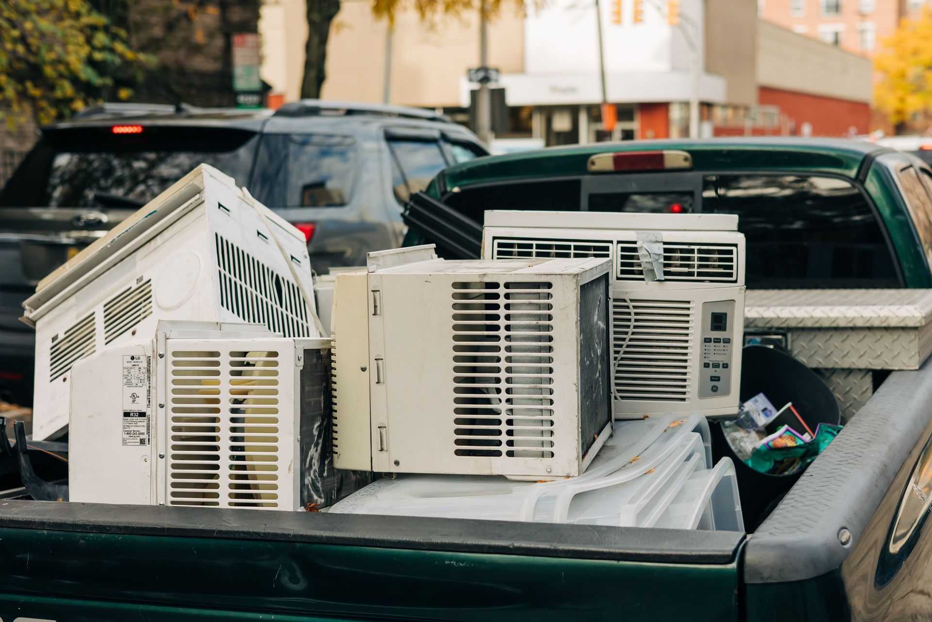 Several window air conditioners stacked in the bed of a pickup truck outdoors