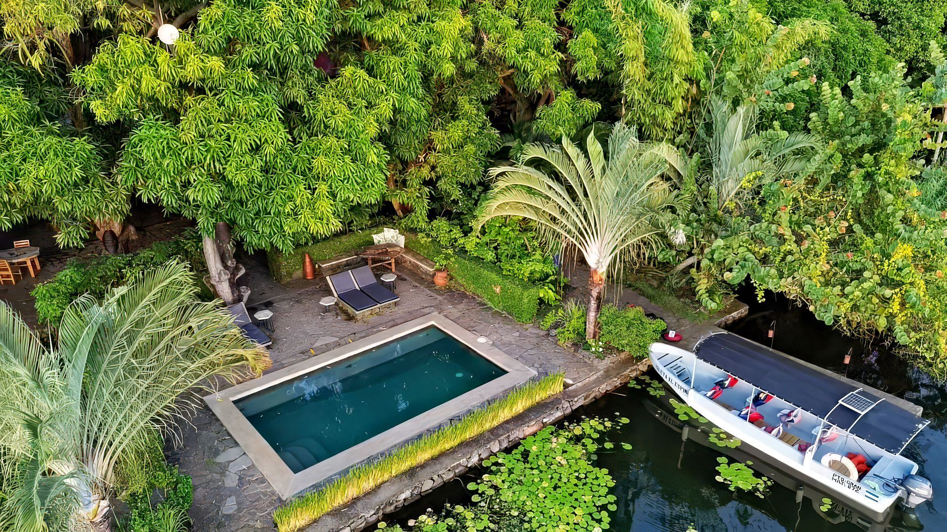 Poolside scene with a boat, surrounded by lush greenery.