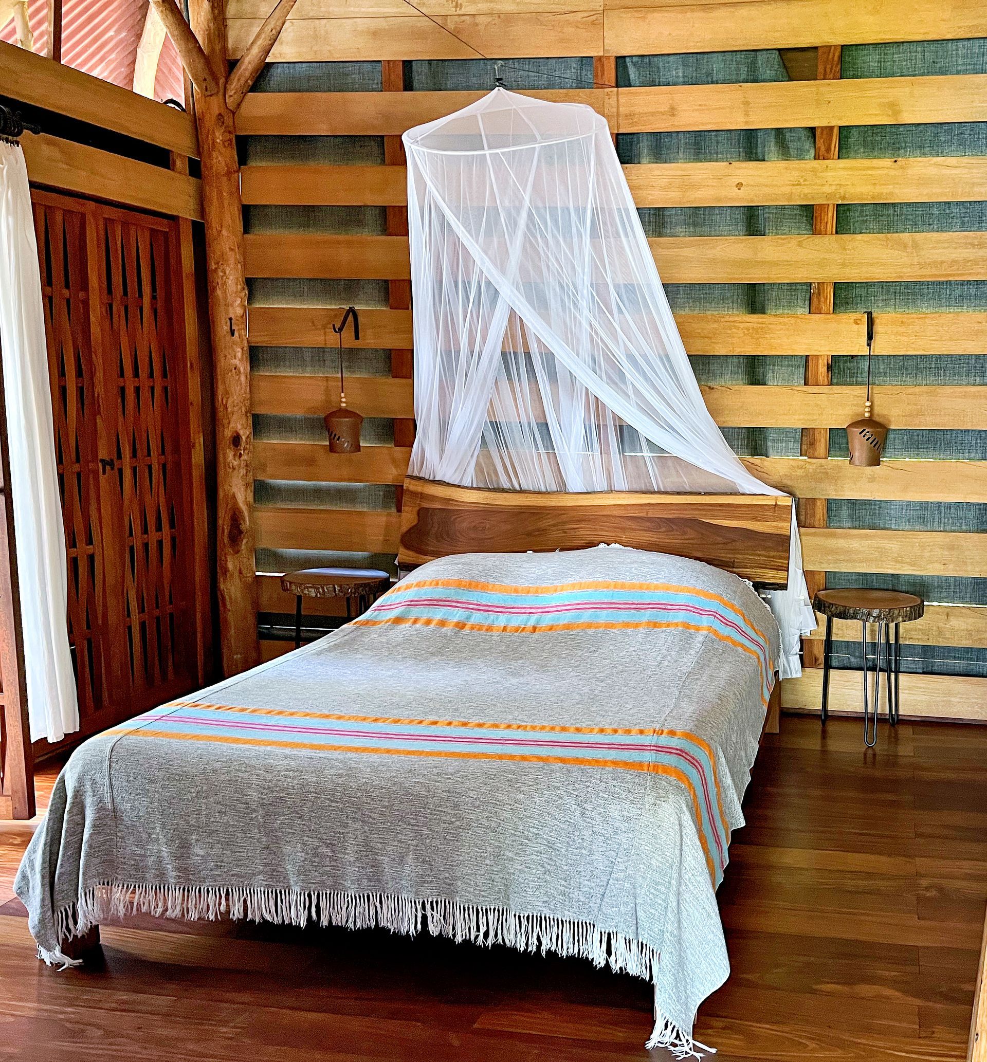 Rustic bedroom with wooden walls, bed with mosquito net, blanket.