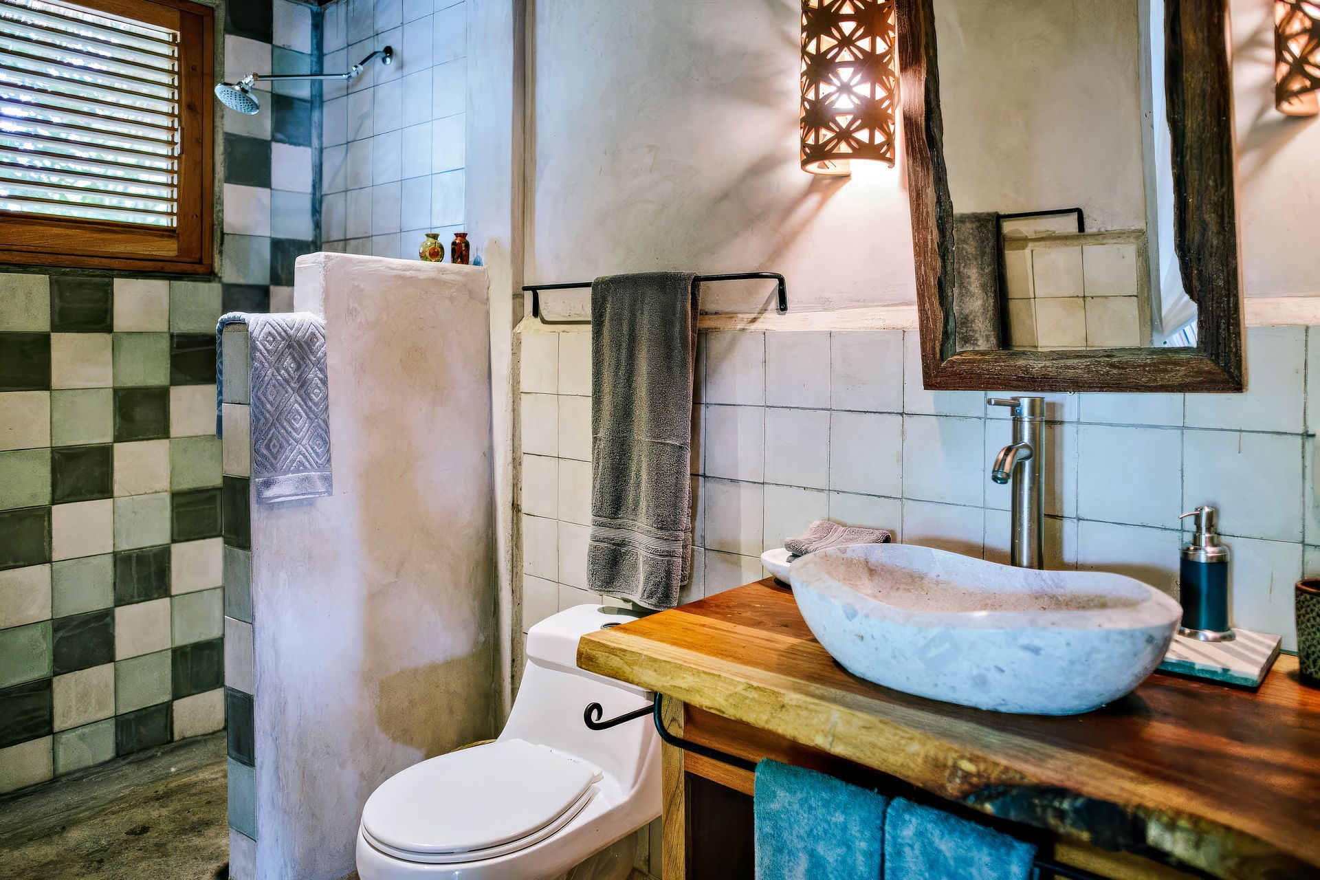 Bathroom with stone sink, wooden counter, white toilet, and green tiled shower.