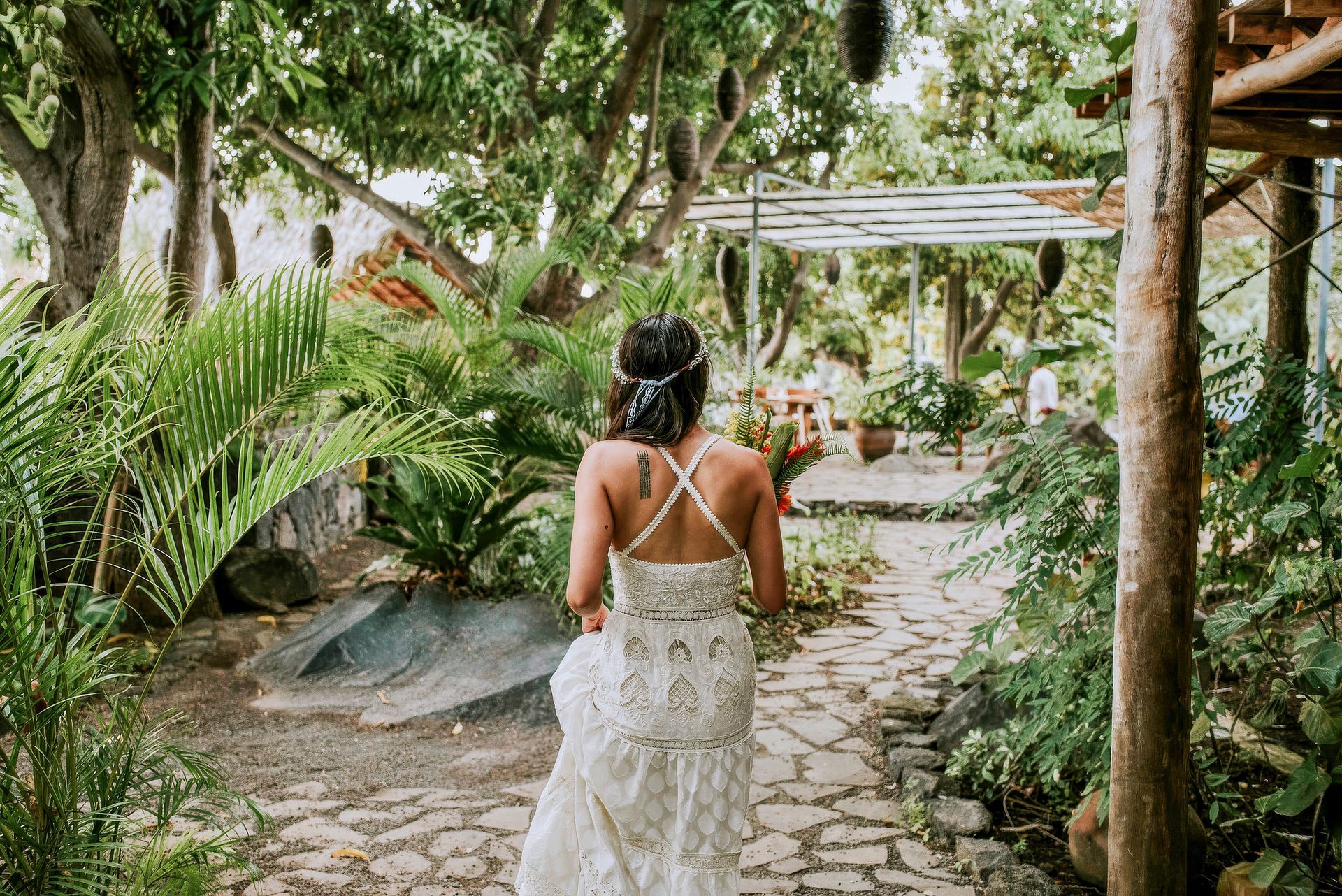 Bride in a white lace dress walks down a stone path in a lush garden.