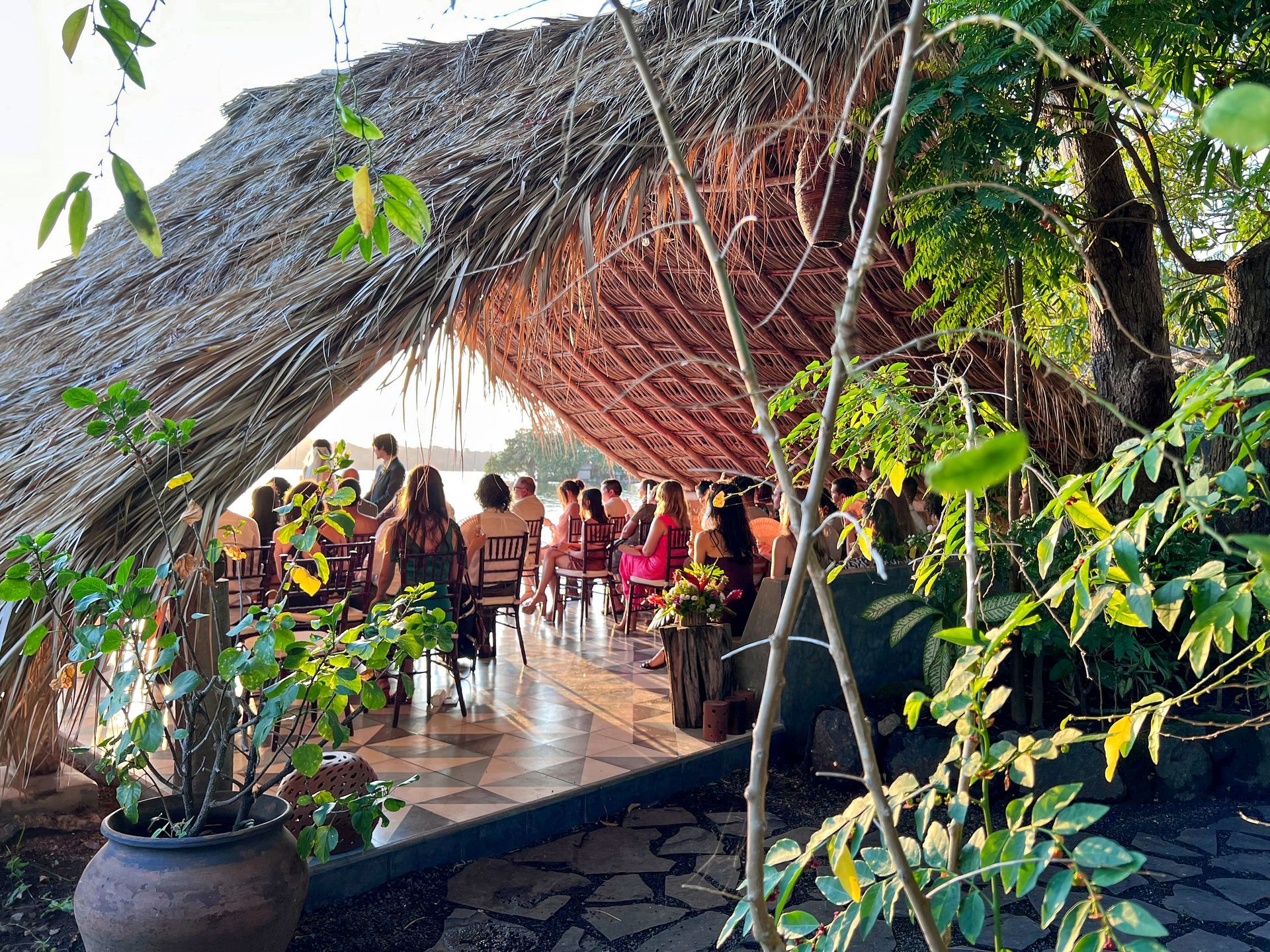 Wedding ceremony under thatched roof; guests seated, facing the waterfront.