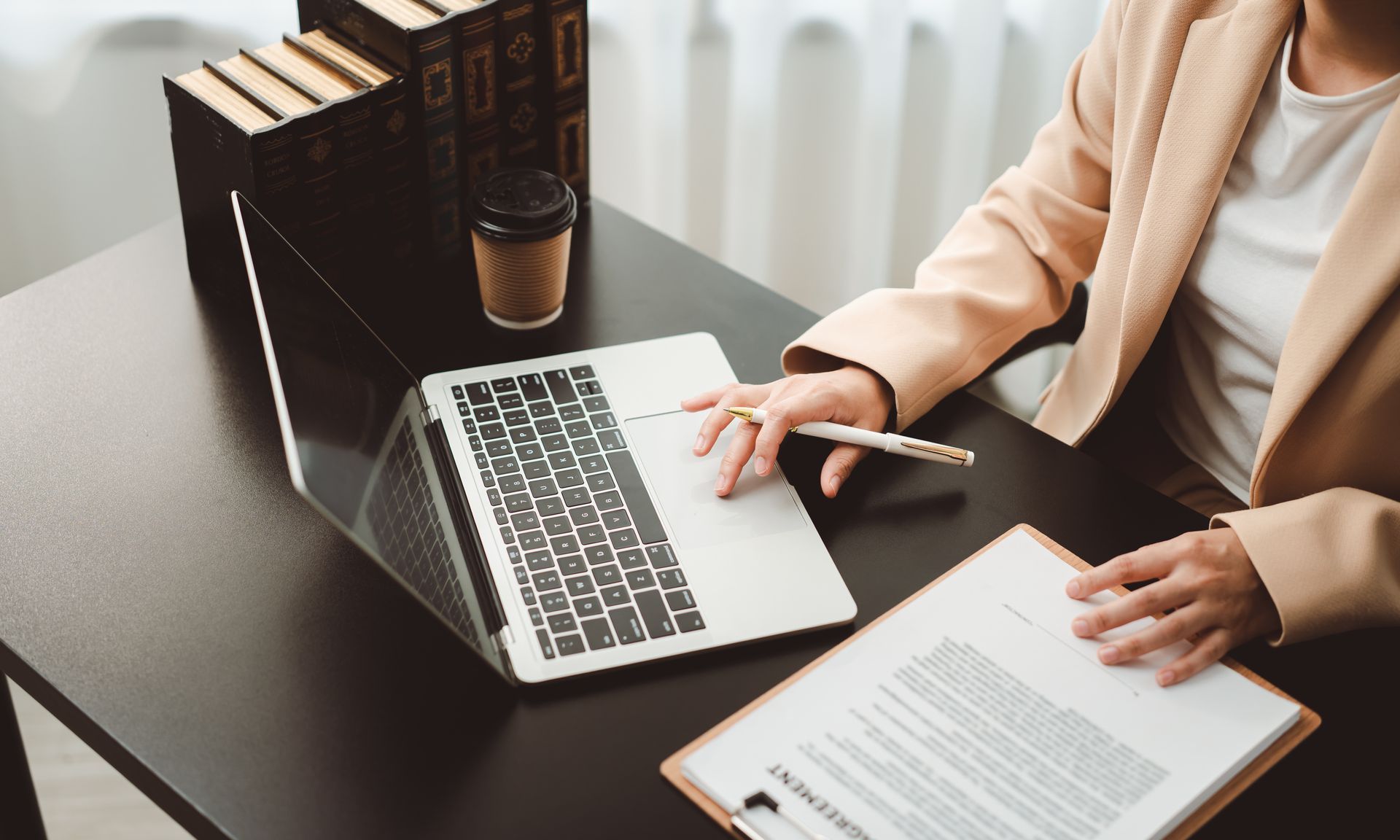 Businesswoman reviewing documents while working on a laptop at her desk