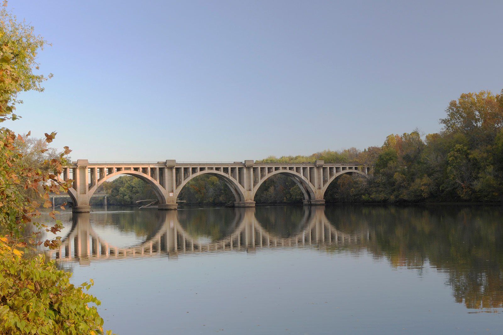 Stone arch bridge over calm river, fall foliage frames.