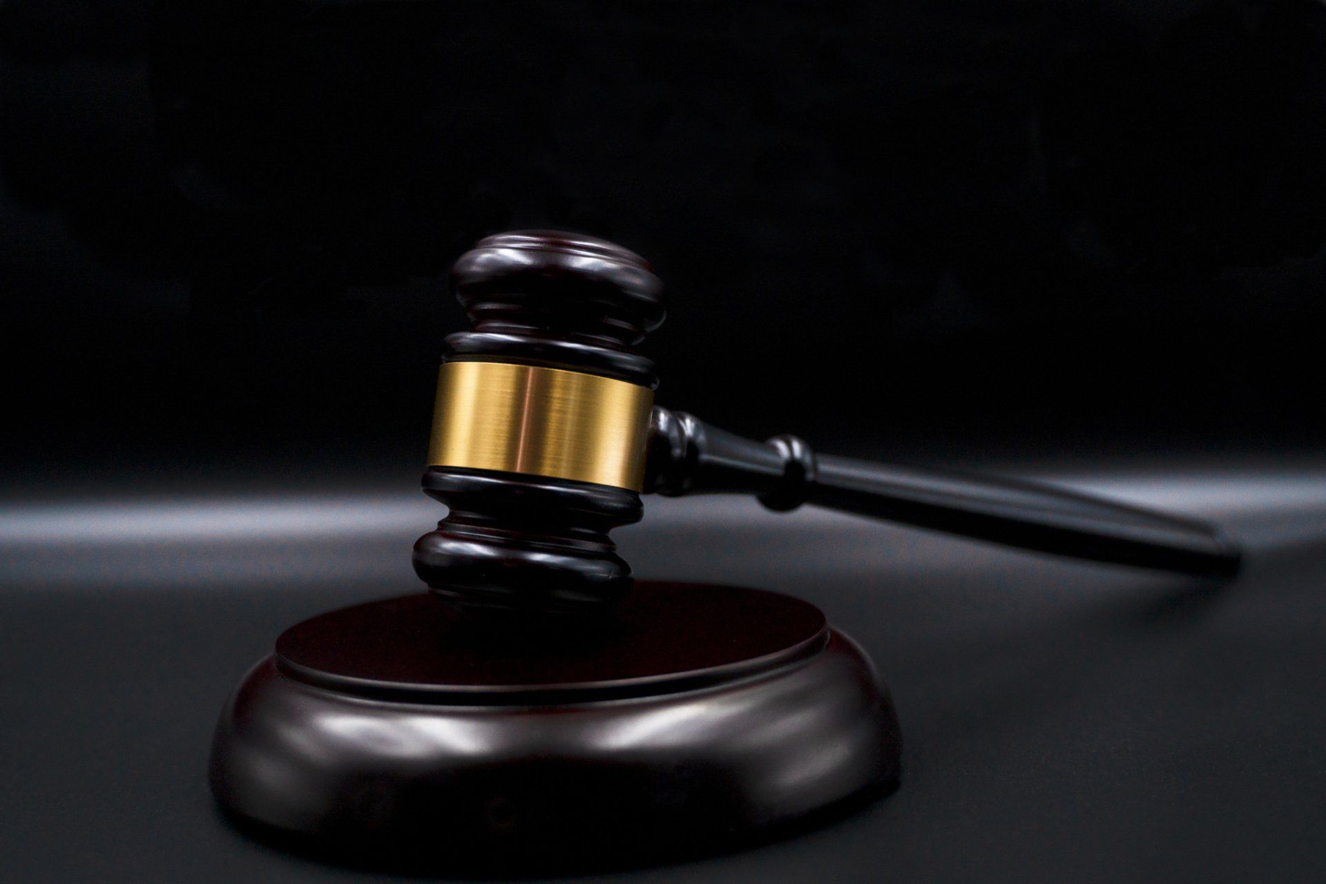 Wooden gavel with gold band on its wooden base against a dark background.