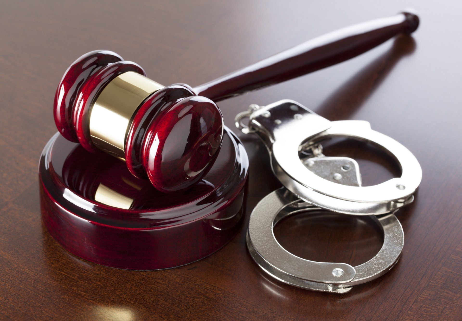 Wooden gavel and open silver handcuffs on a brown wooden surface.