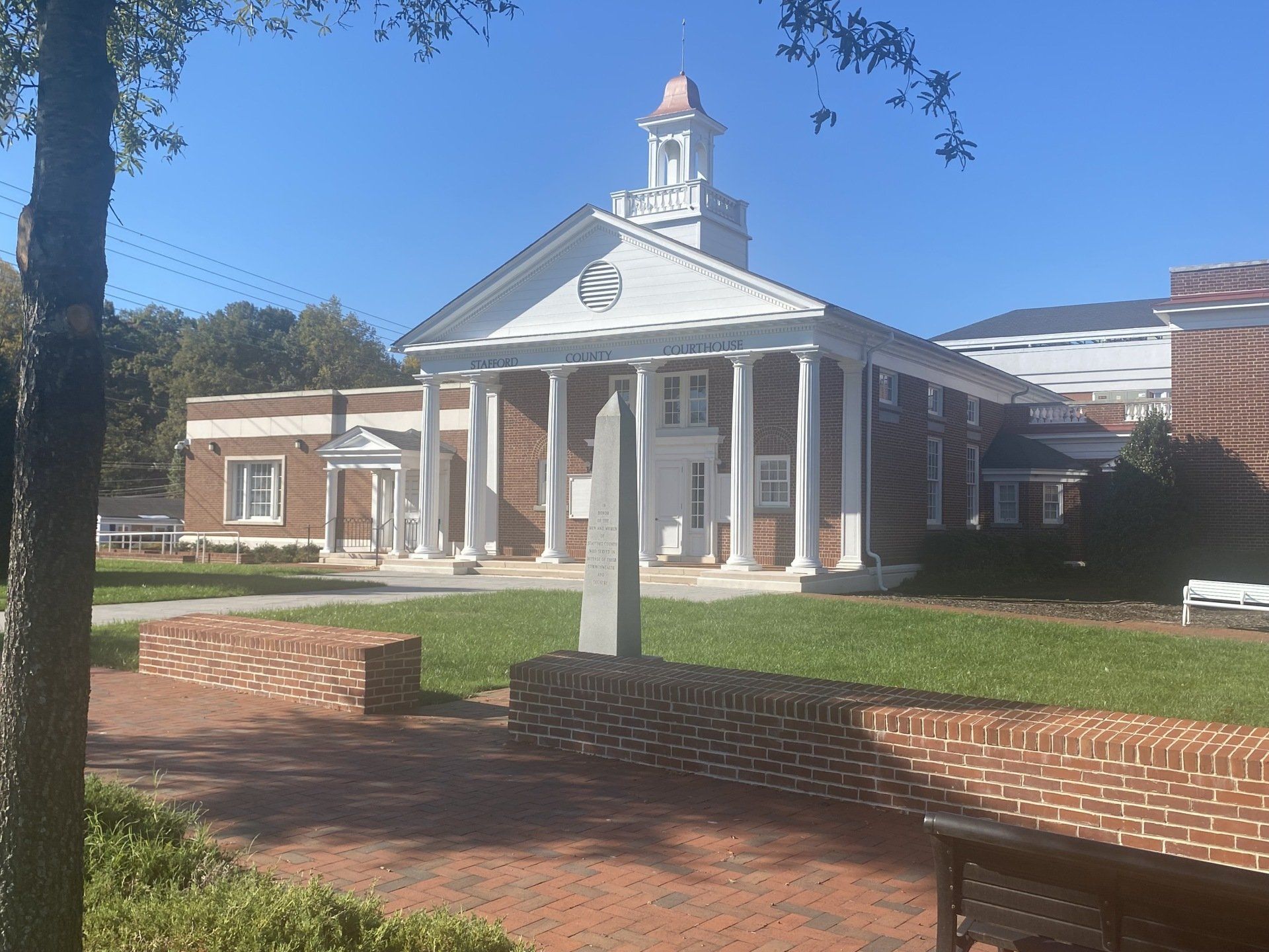 Brick building with white columns and a cupola on a green lawn, brick walkway in front.