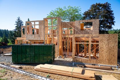Construction site of a two-story house framed with wood. A large green dumpster sits in front.