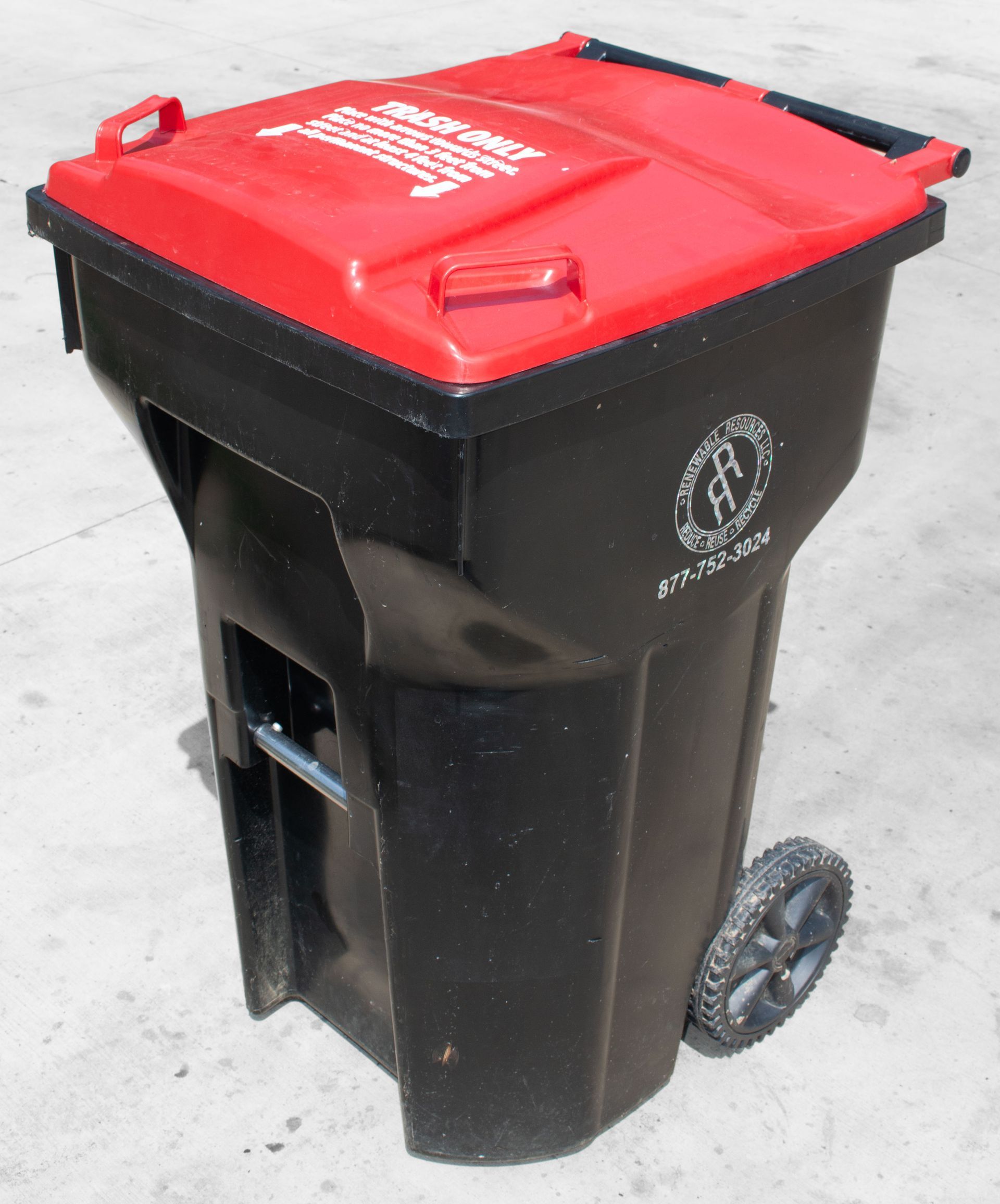 Black and red wheeled trash bin, with a logo, on a concrete surface. 65 gallon trash container.