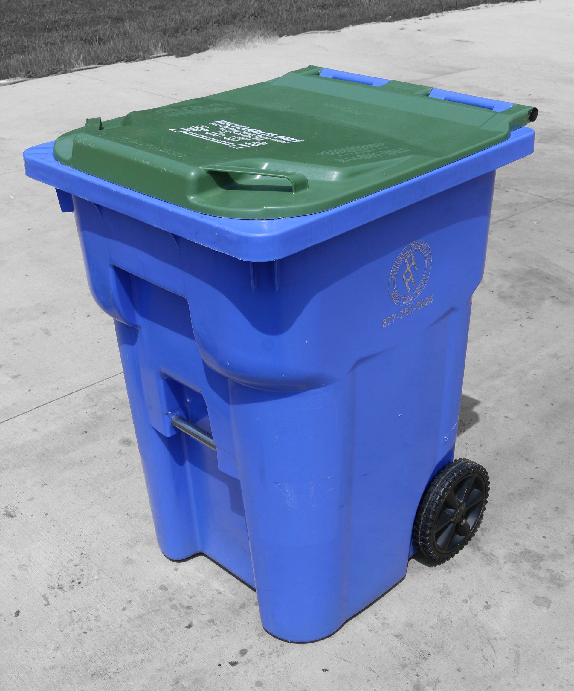 Blue recycling bin with a green lid and a black wheel, on a gray concrete surface. 95 gallon trash container.