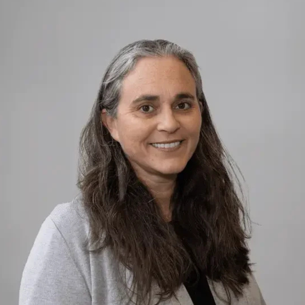 Woman in academic robes smiles, wearing a Māori woven stole, in front of a patterned backdrop.