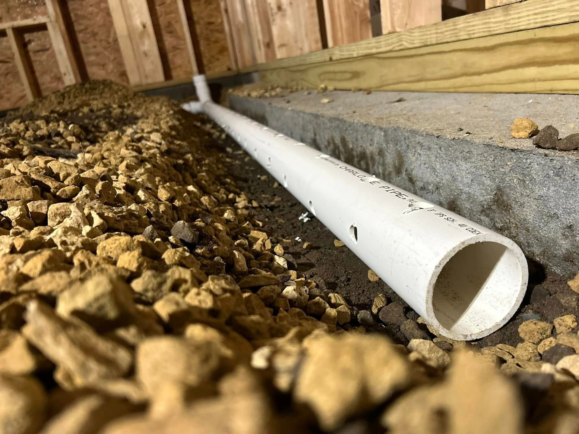 White PVC pipe surrounded by gravel, running along a concrete foundation inside a structure.
