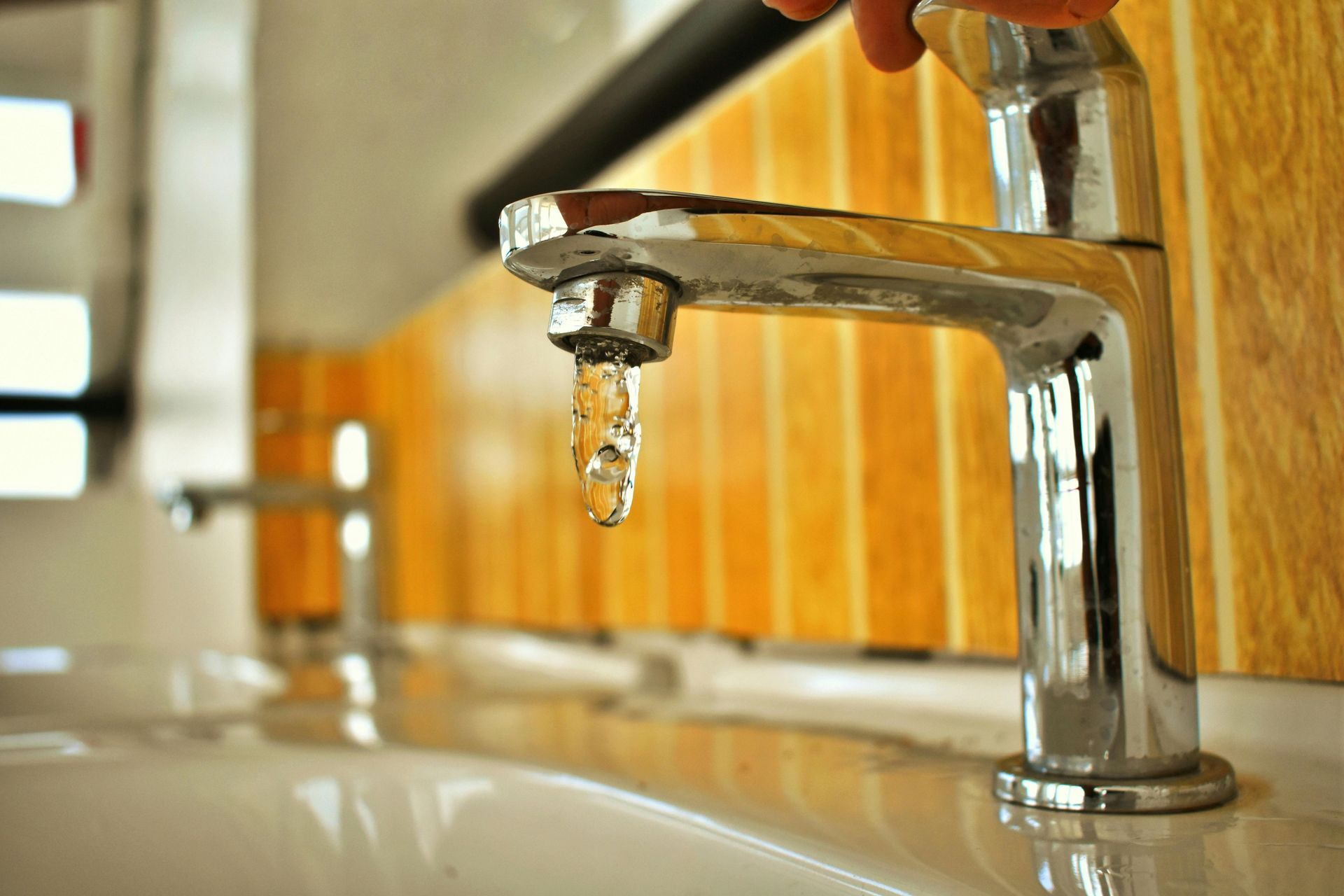 Faucet with water dripping in a bathroom, with a second faucet visible in the background.