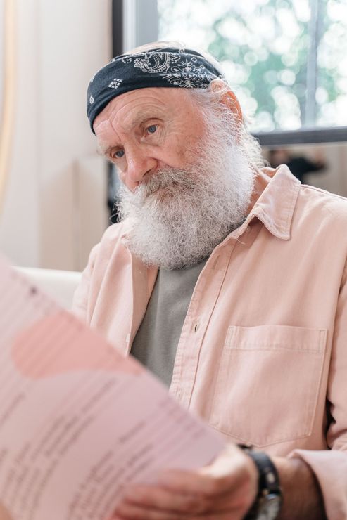 Bearded person in a bandana reading papers by a window in a bright room