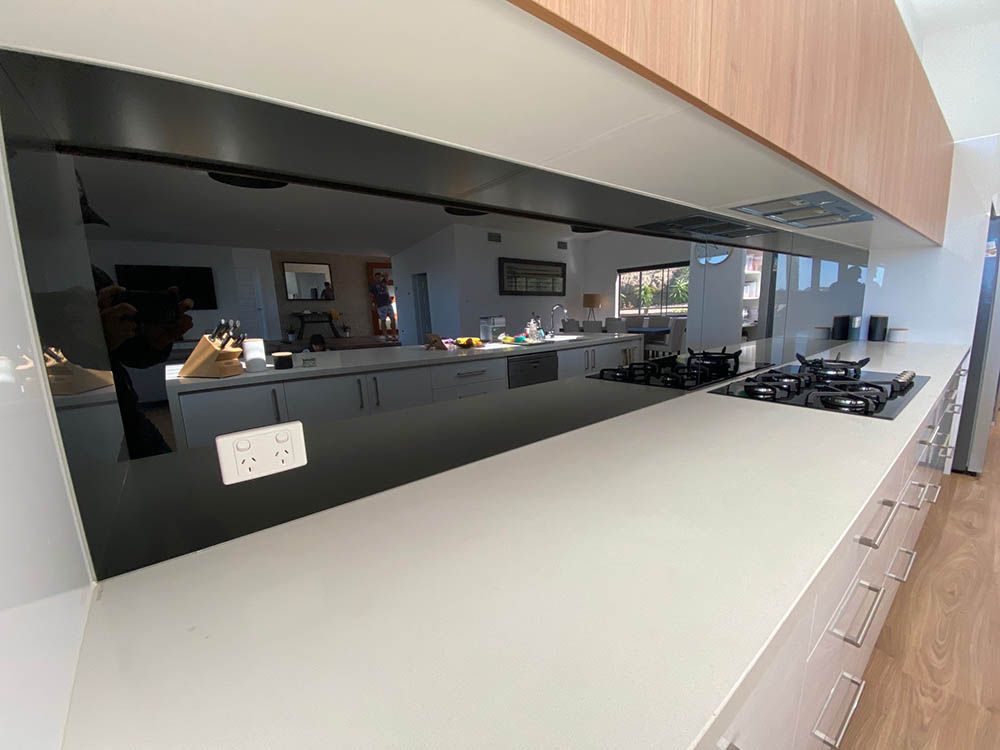 A Kitchen With a Stove Top Oven, a Sink, and a Mirrored Backsplash — Reflect Glass In Gosford, NSW