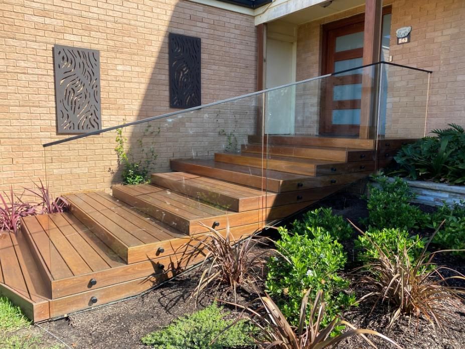 A Wooden Deck With Stairs and a Glass Railing in Front of a Brick House — Reflect Glass In Tuggerah, NSW