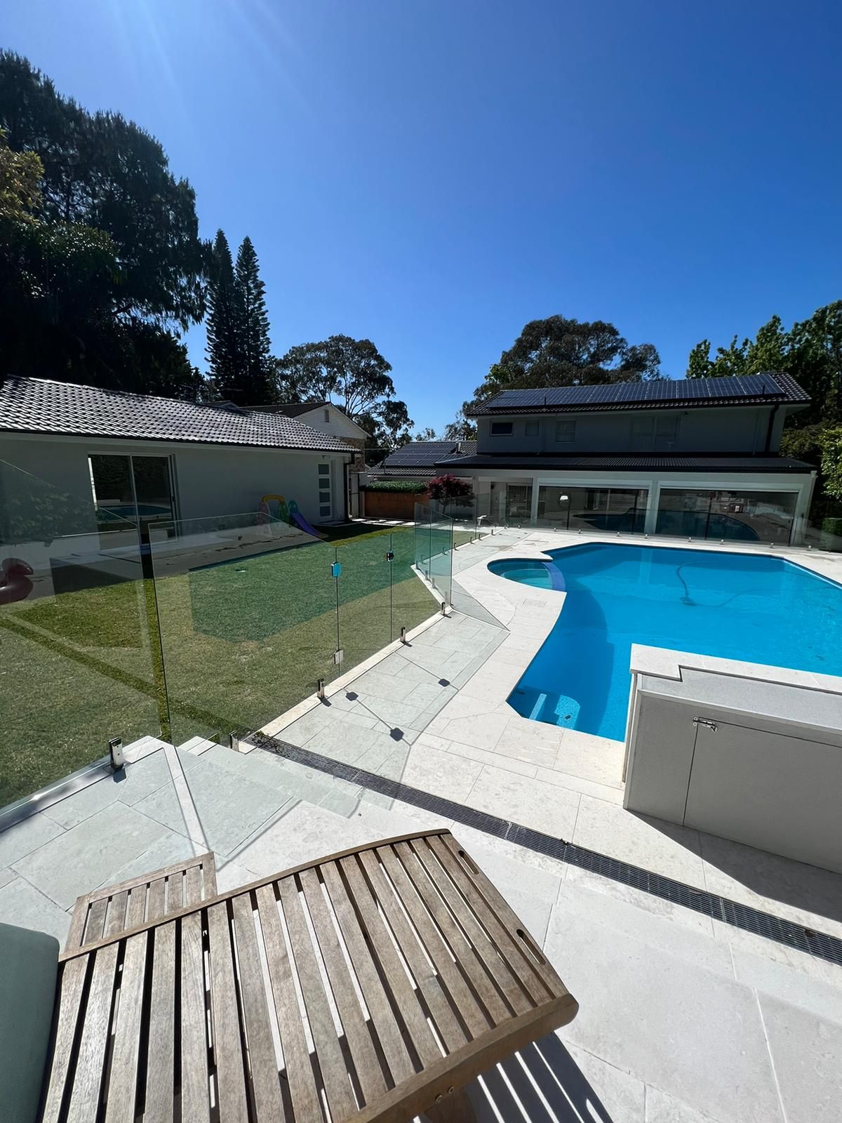 A Large Swimming Pool is Surrounded by a Glass Fence and a Wooden Deck — Reflect Glass In Gosford, NSW