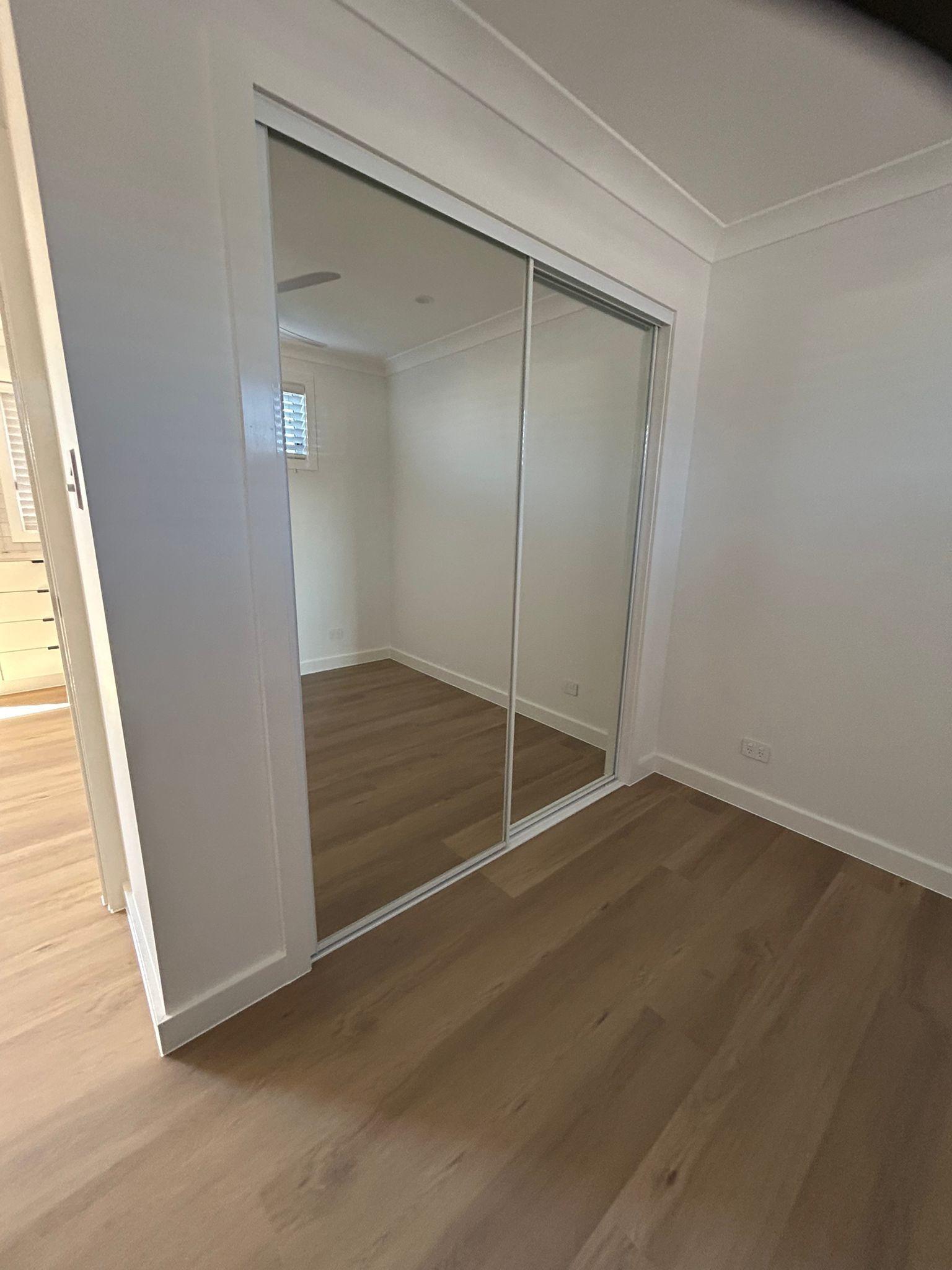 An Empty Bedroom With a Large Sliding Wardrobe and a Window — Reflect Glass In Tuggerah, NSW