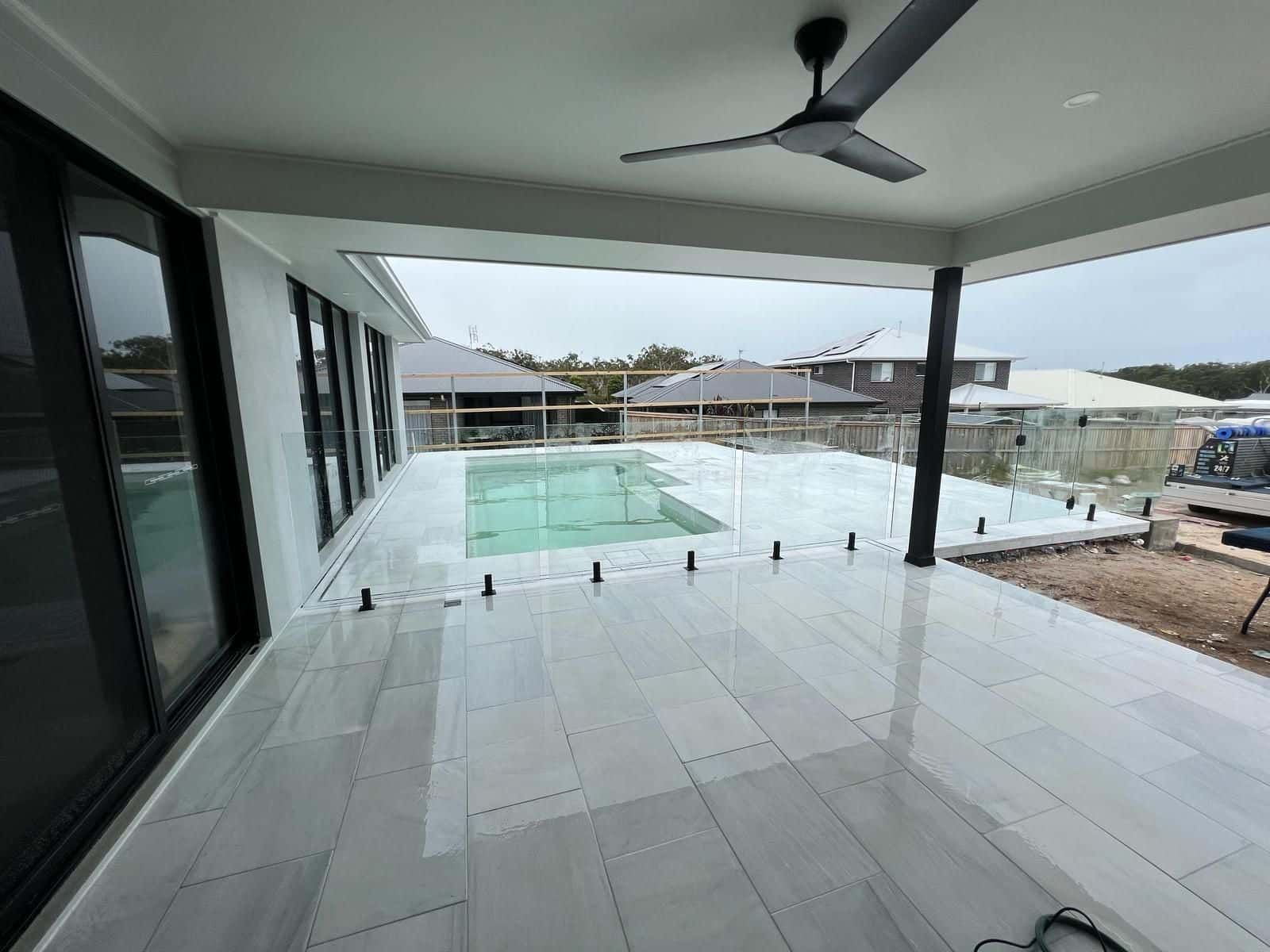 A Small Swimming Pool Surrounded by a Glass Fence and a Wooden Deck — Reflect Glass In Tuggerah, NSW