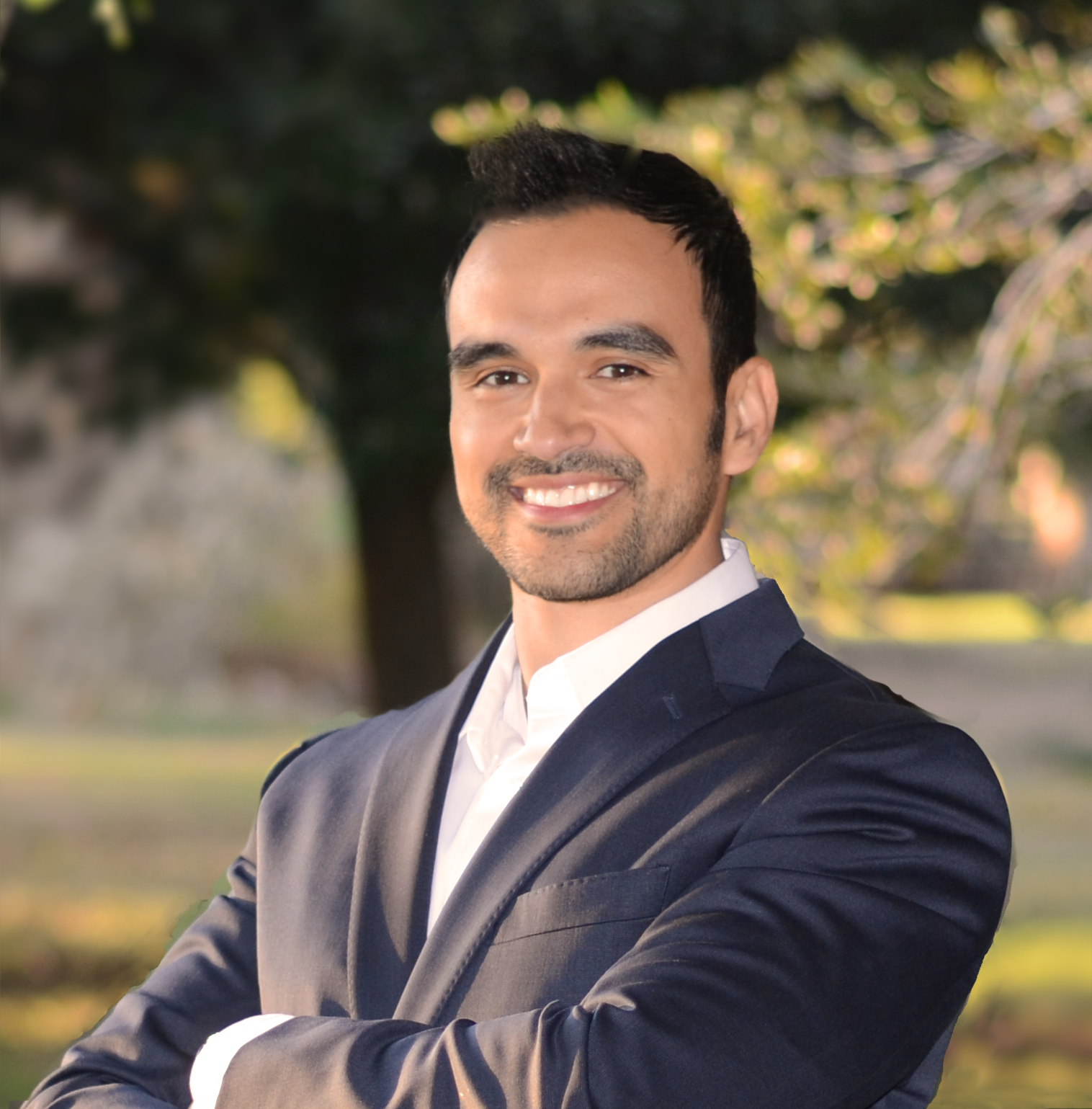 A man in a suit is smiling with his arms crossed