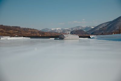 A bridge over a frozen lake with mountains in the background.
