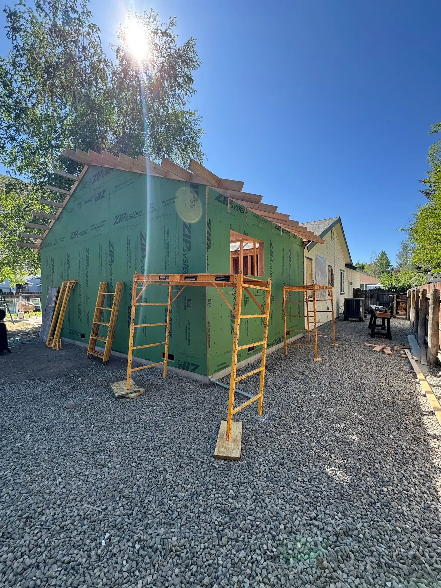 Green house under construction with scaffolding, gravel ground, and a blue sky backdrop