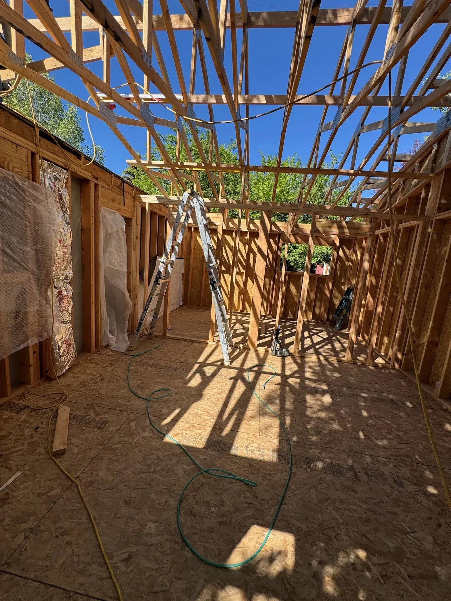 Damaged room with exposed wooden beams, torn wall panels, and sunlight casting shadows on the dirt floor.