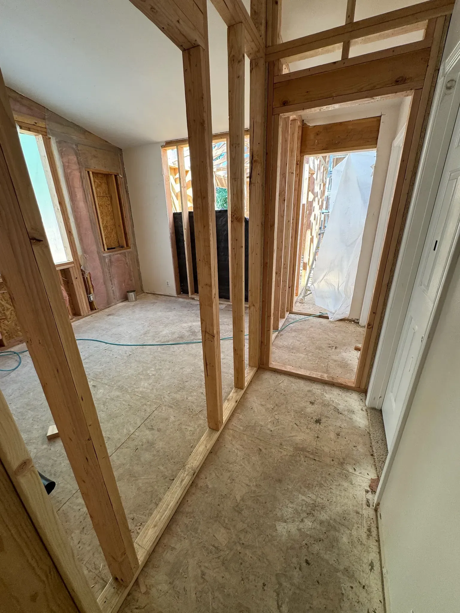 Unfinished hallway with exposed wooden framing, bare drywall, and carpeted floor under construction.