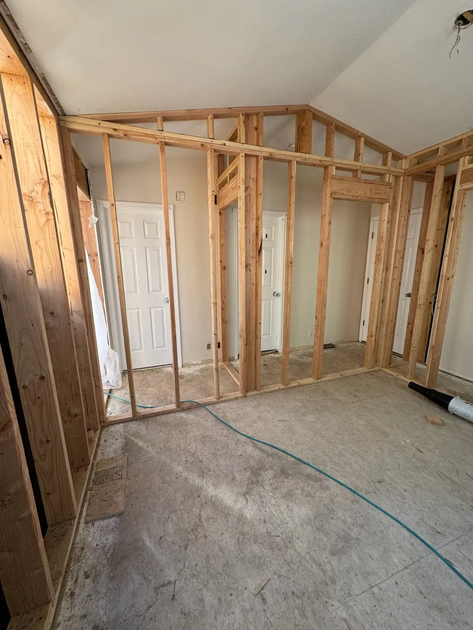 Exposed wooden framing in an unfinished room with carpet and a closed white door.