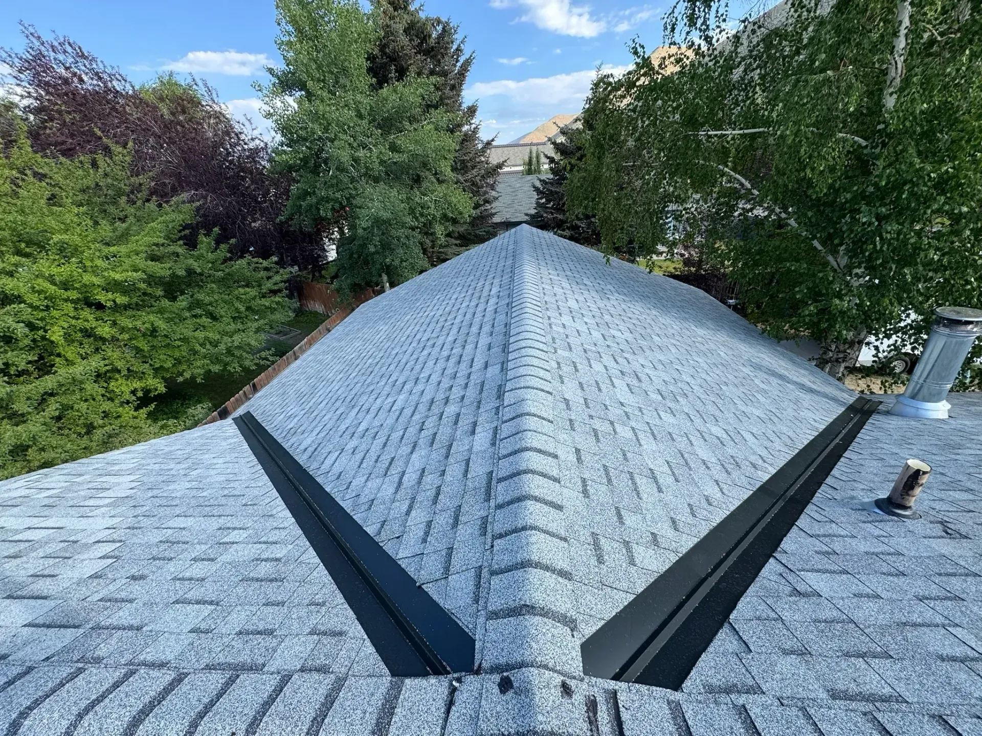 Gray shingled roof with central ridge, framed by green trees under a blue sky