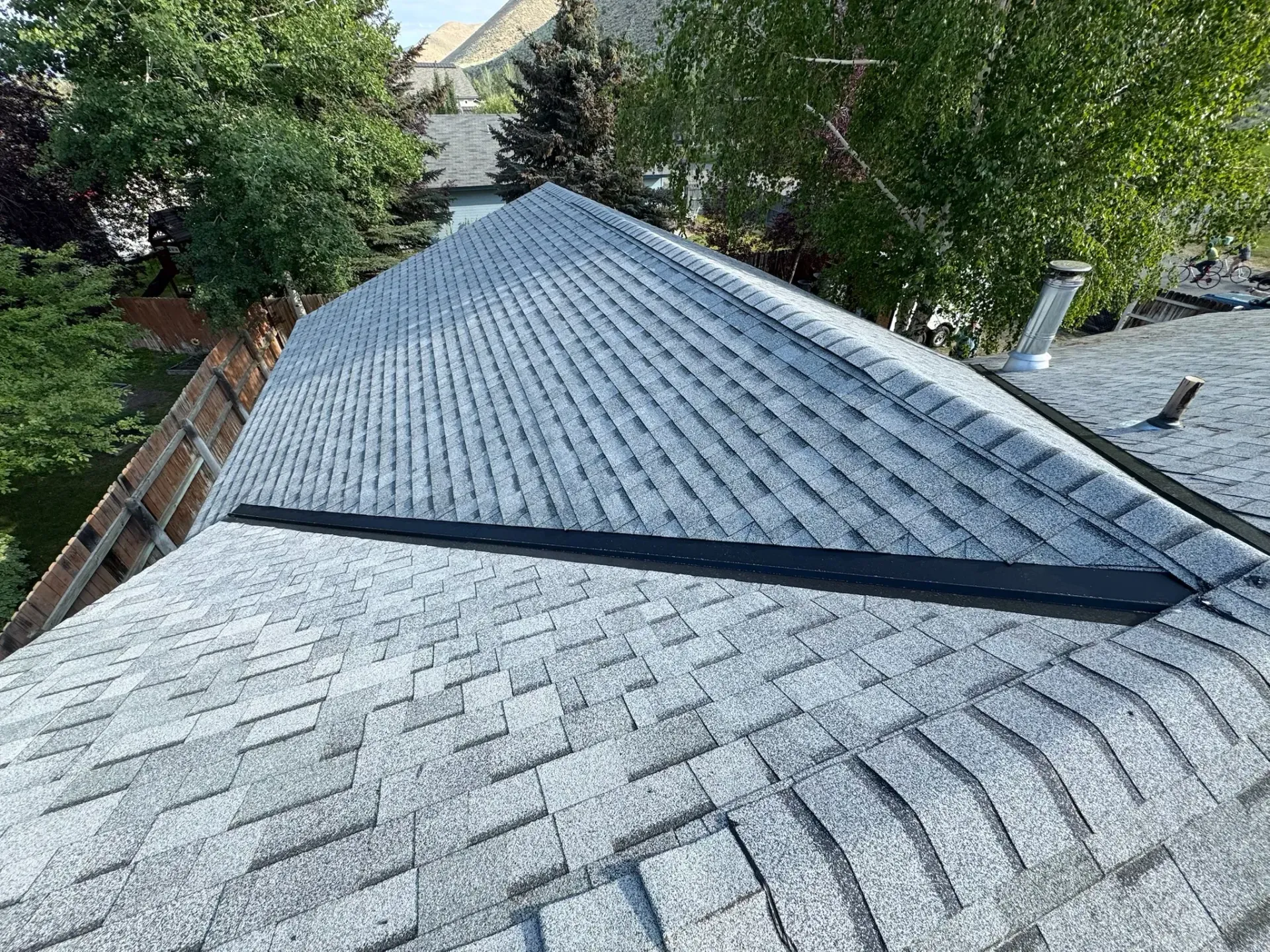 Steep gray shingled roof with a dark ridge vent, surrounded by green trees