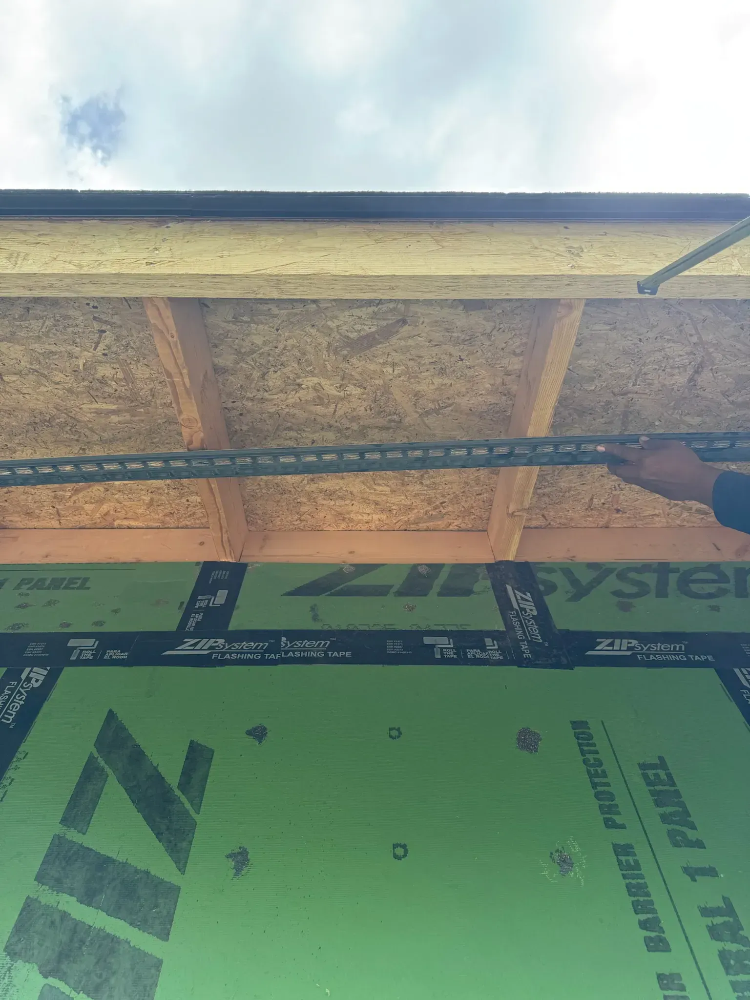 Insulation and wood framing beneath a roof, with green underlayment in the foreground.