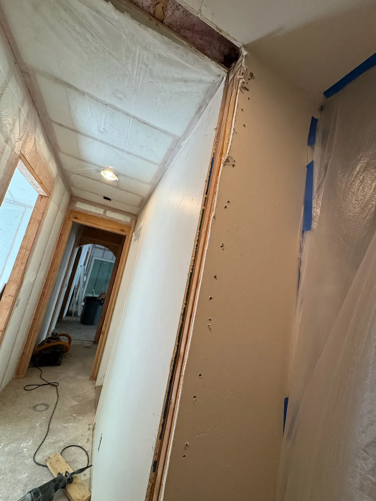 Narrow hallway under renovation with plastic-covered walls, exposed trim, and cables on the floor