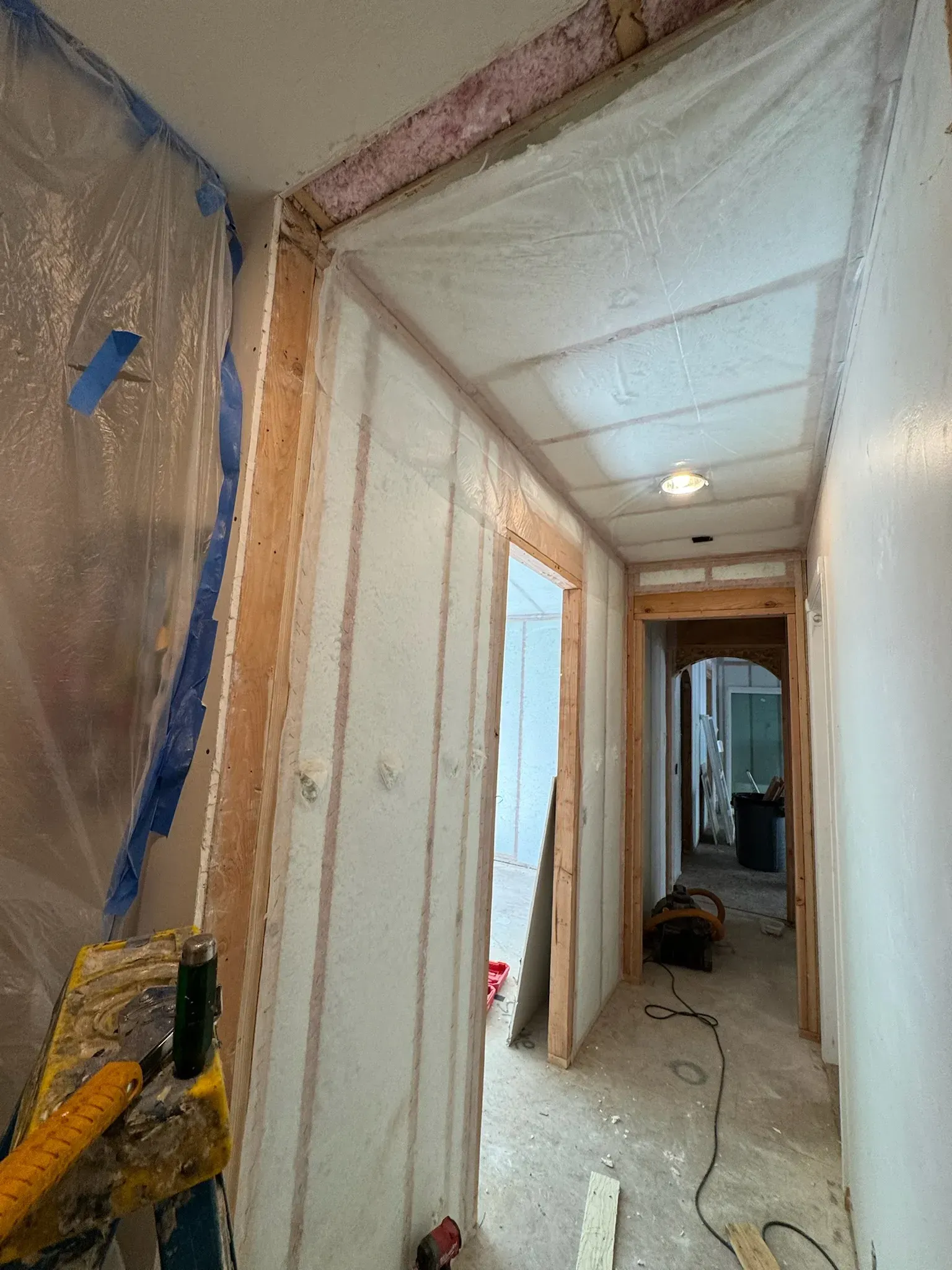 Narrow hallway under renovation with drywall, exposed insulation, tools, and construction debris on the floor