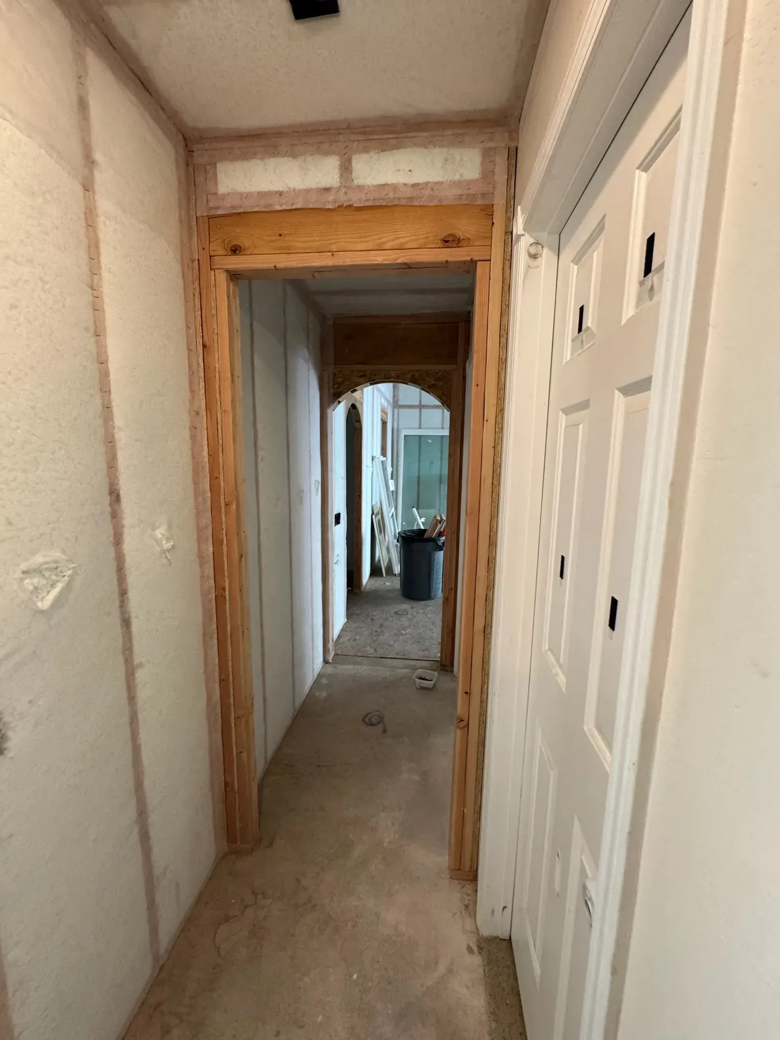 Narrow unfinished hallway with exposed framing, white doors, and debris on the floor