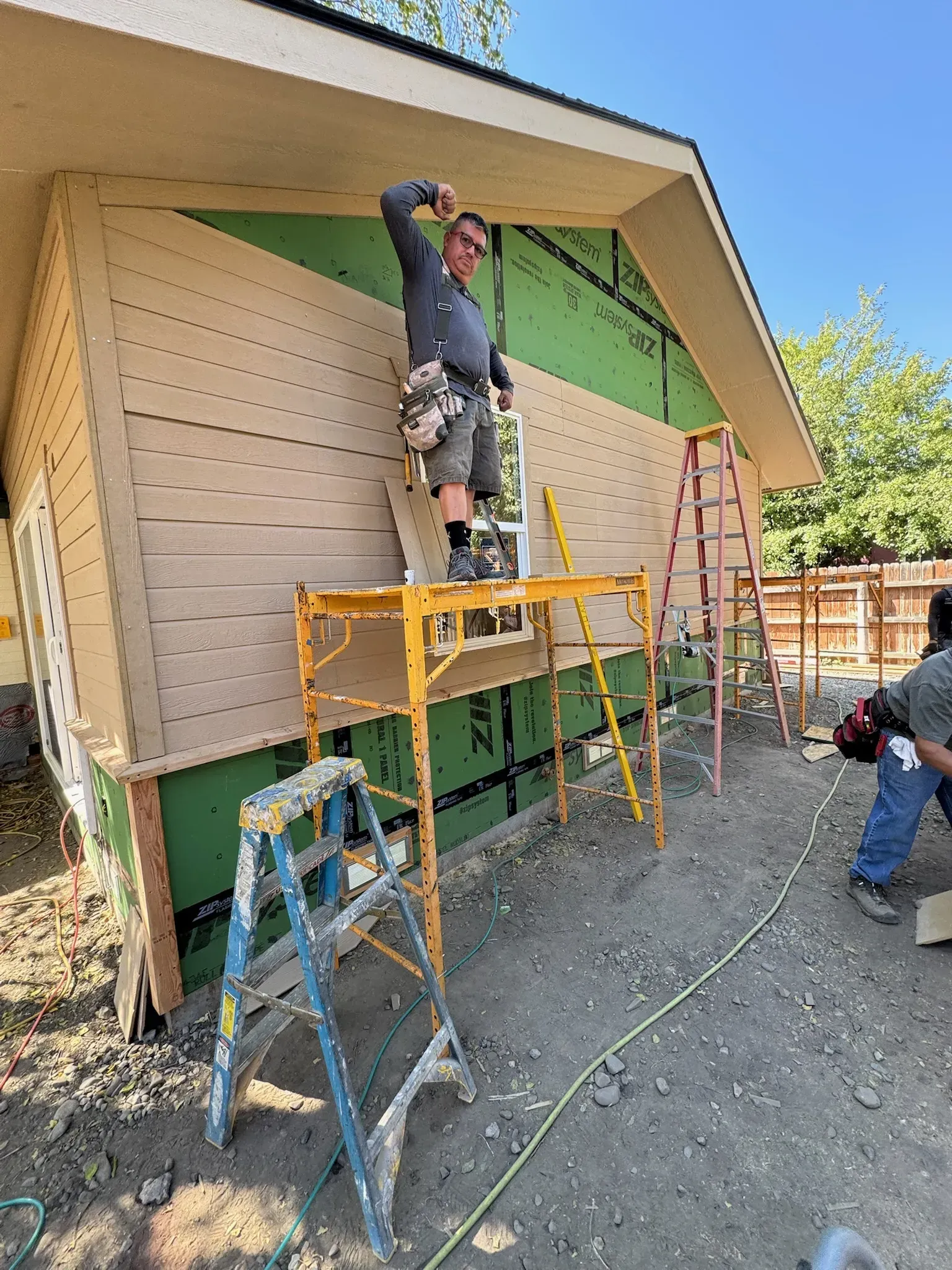 Worker standing on scaffolding painting a building exterior beside ladders and green trim