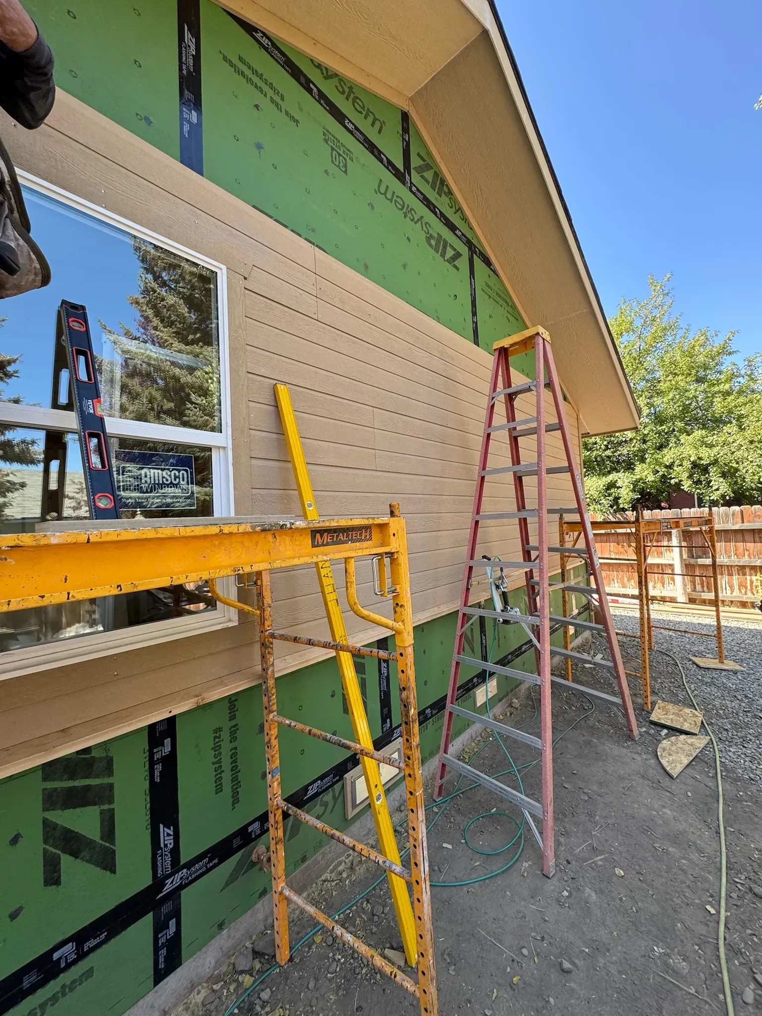 Construction workers installing beige siding on a house exterior with ladders and scaffolding