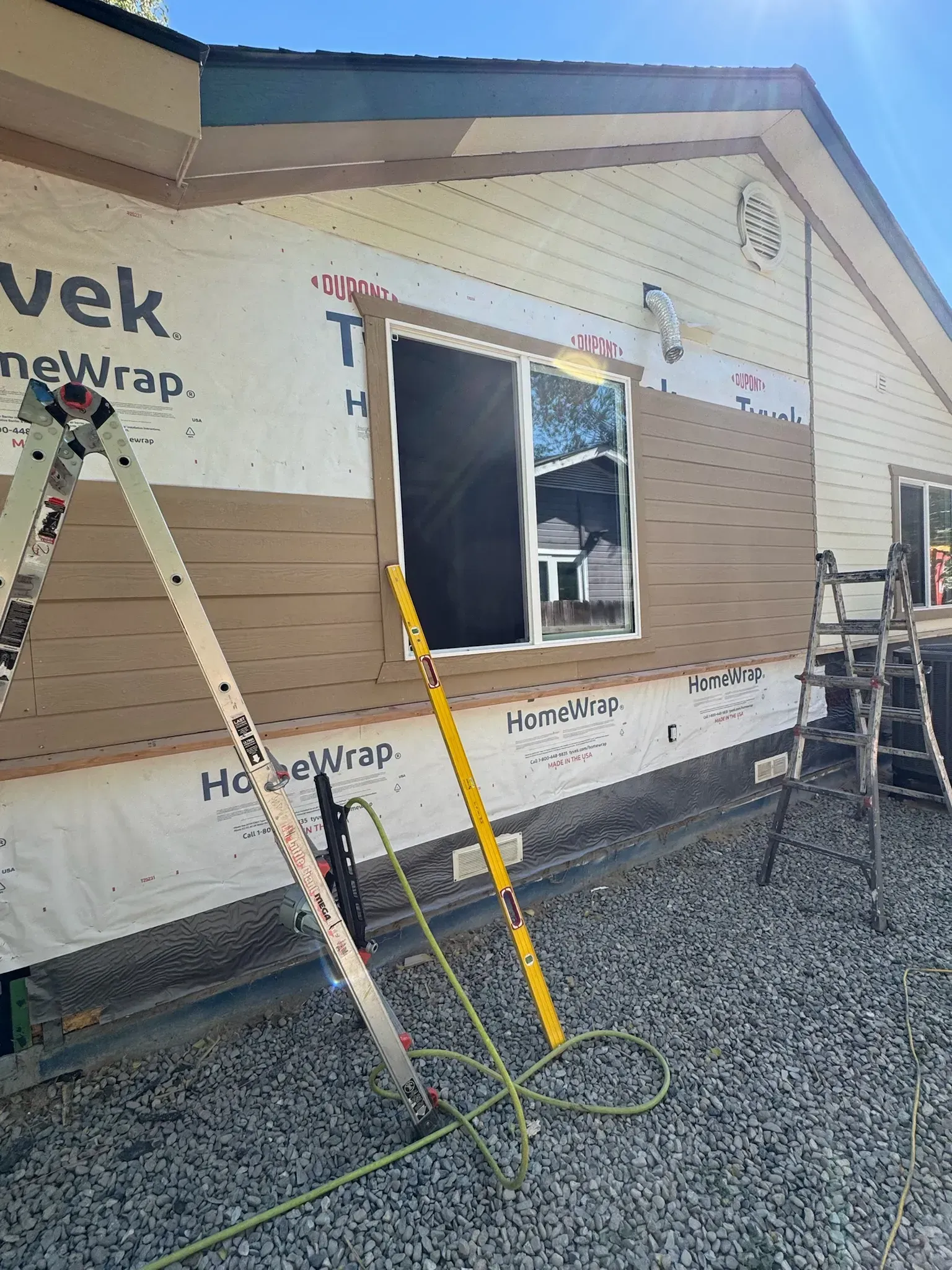 Construction site with ladder, window opening, and house wrap on an exterior wall